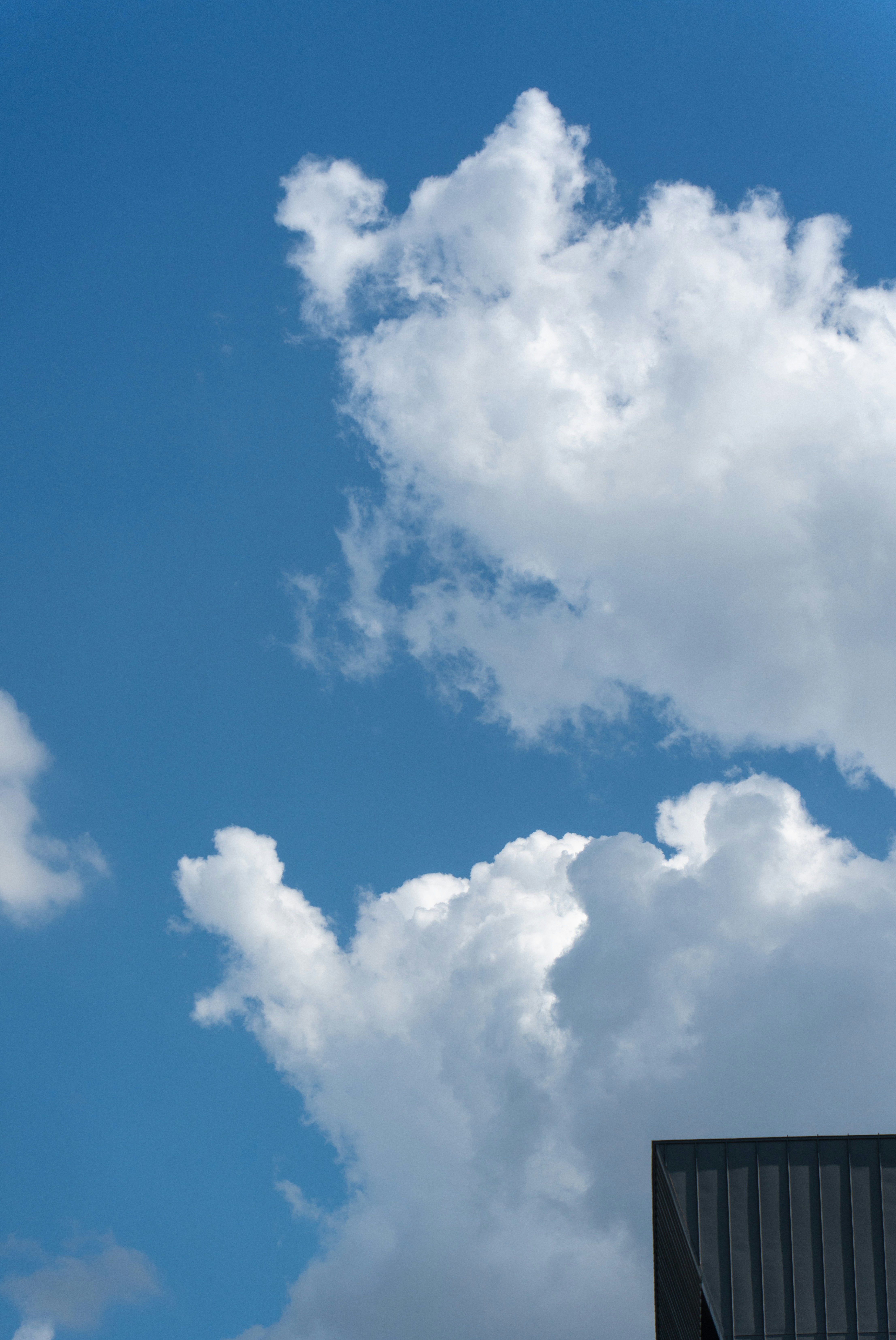 White cumulus clouds in a bright blue sky above a dark metal roof.
