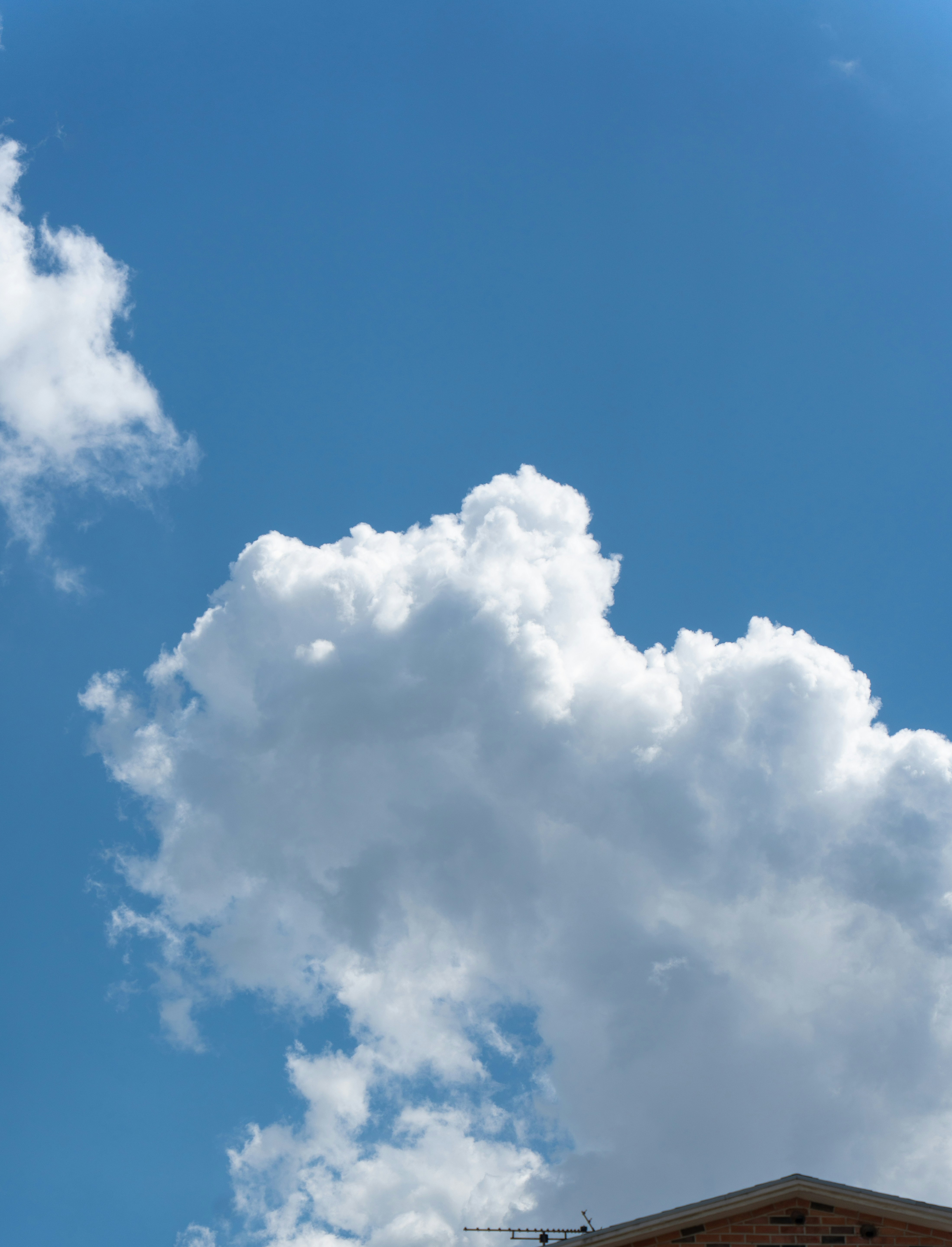 White cumulus clouds drifting across a bright blue sky above a brick roof.