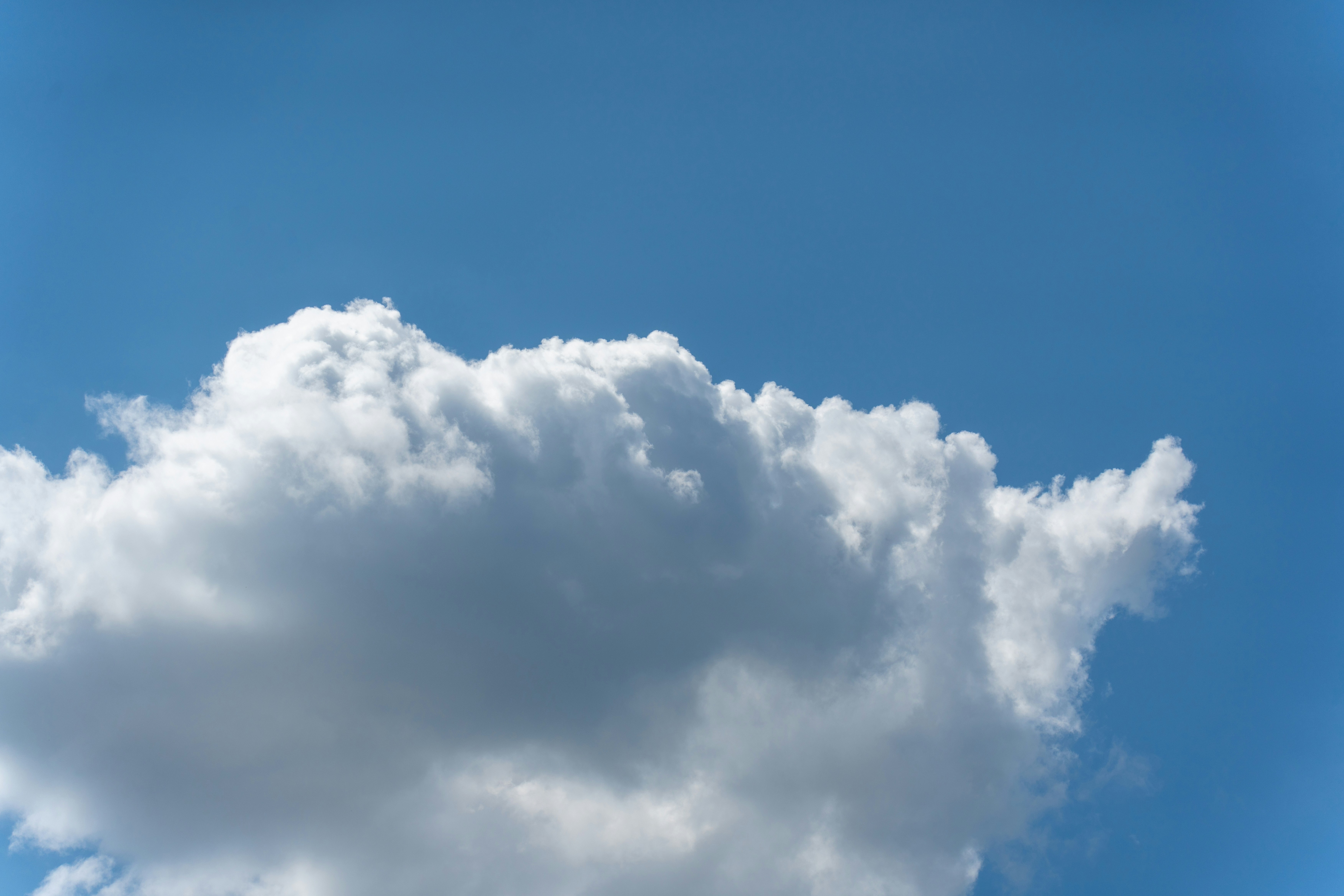 A single white cumulus cloud against a clear blue sky.
