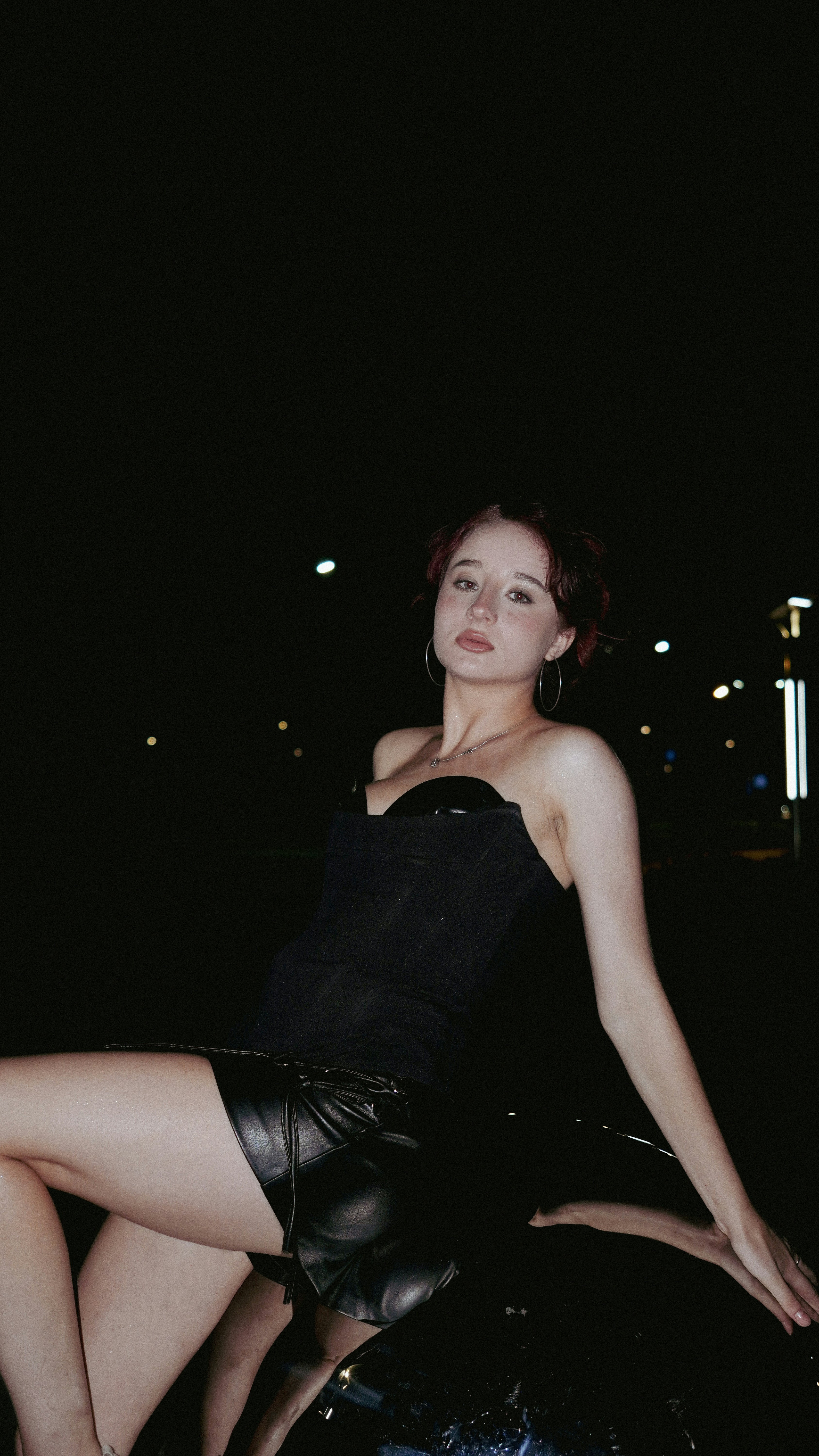 A woman in a black corset and leather skirt against a dark night background