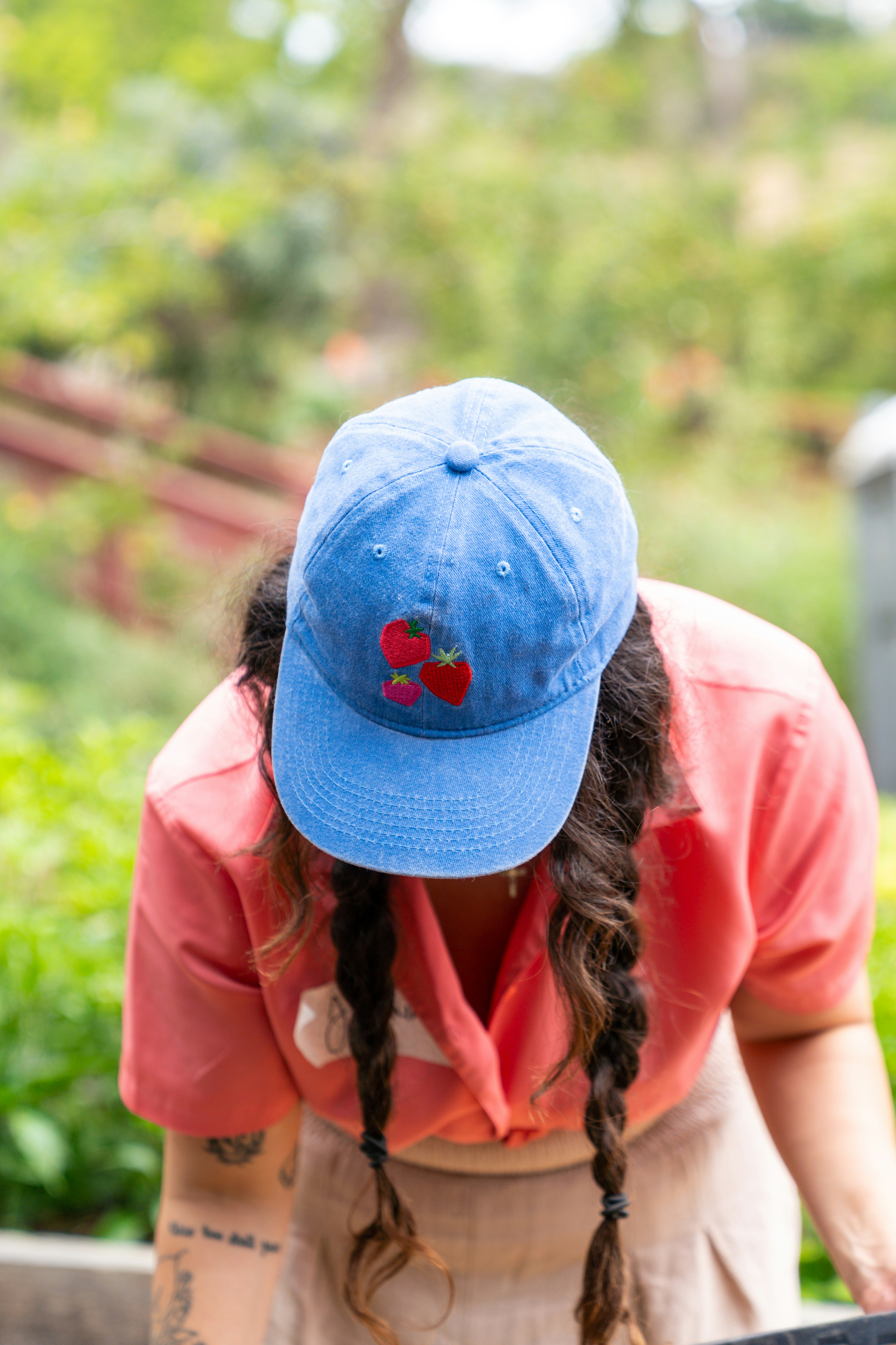 A person wearing a blue baseball cap with strawberry embroidery and a coral shirt
