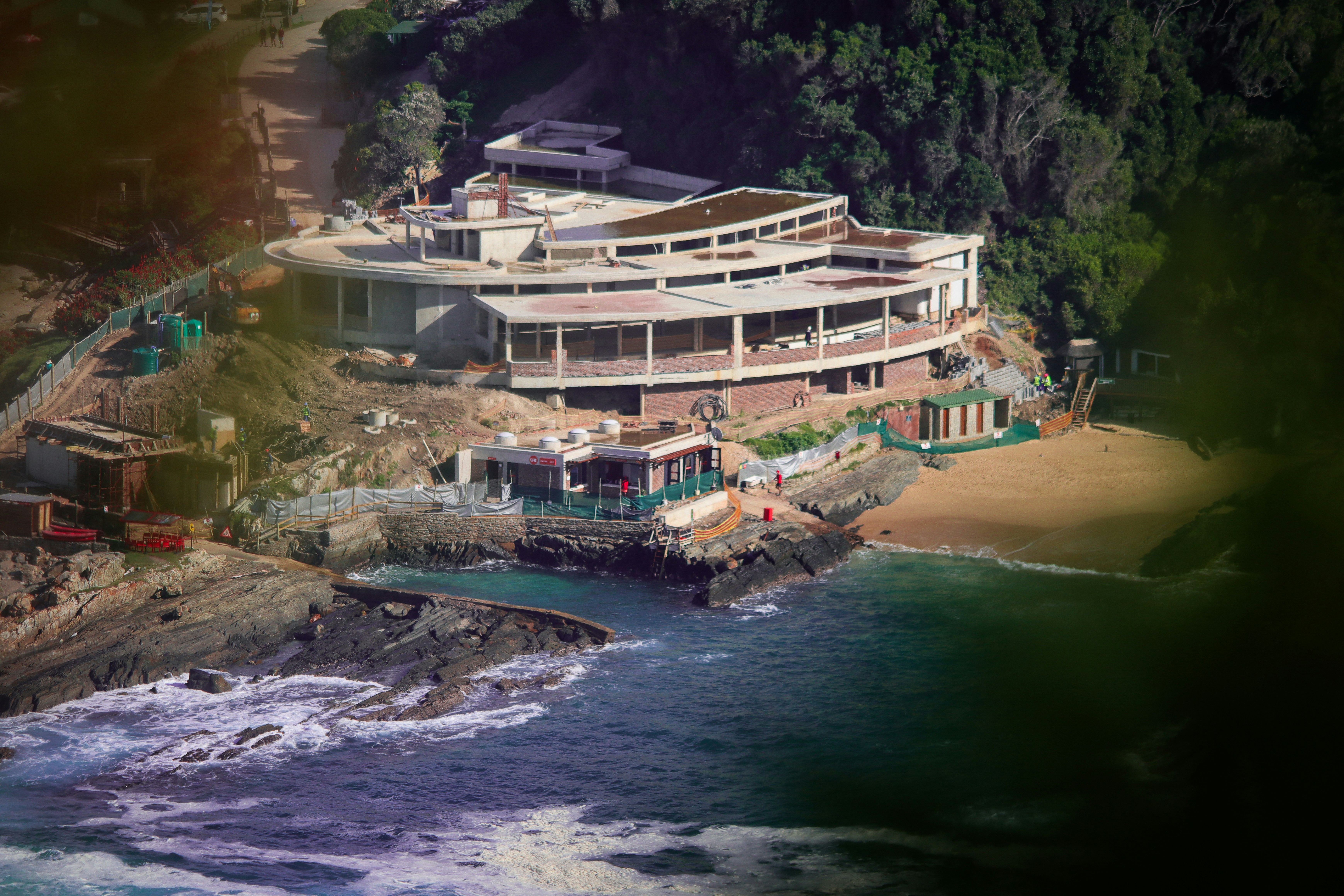 An aerial view of a large concrete building under construction on a rocky coastline