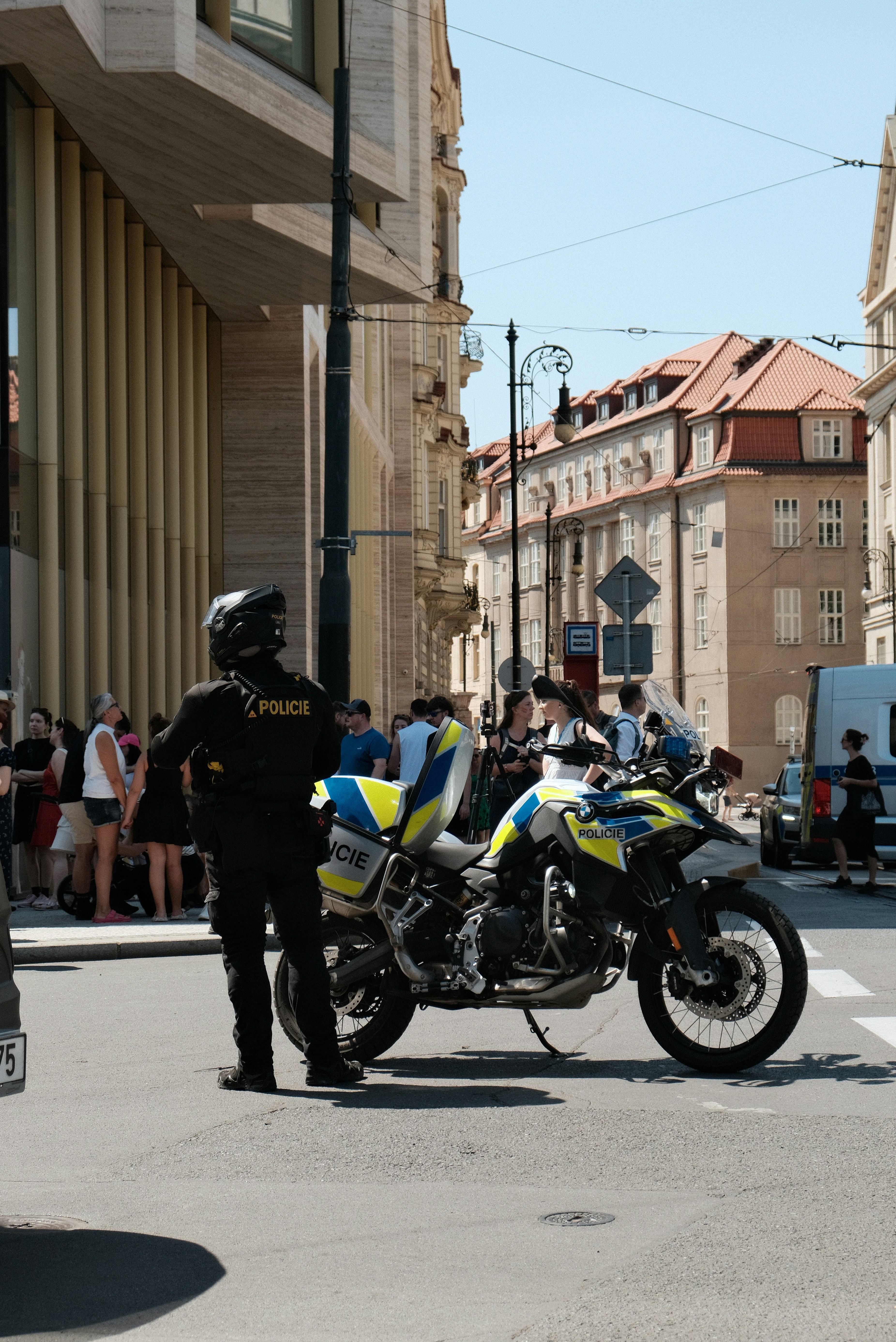 Ein Polizist in schwarzer Ausrüstung steht neben einem Motorrad auf einer Prager Straße.