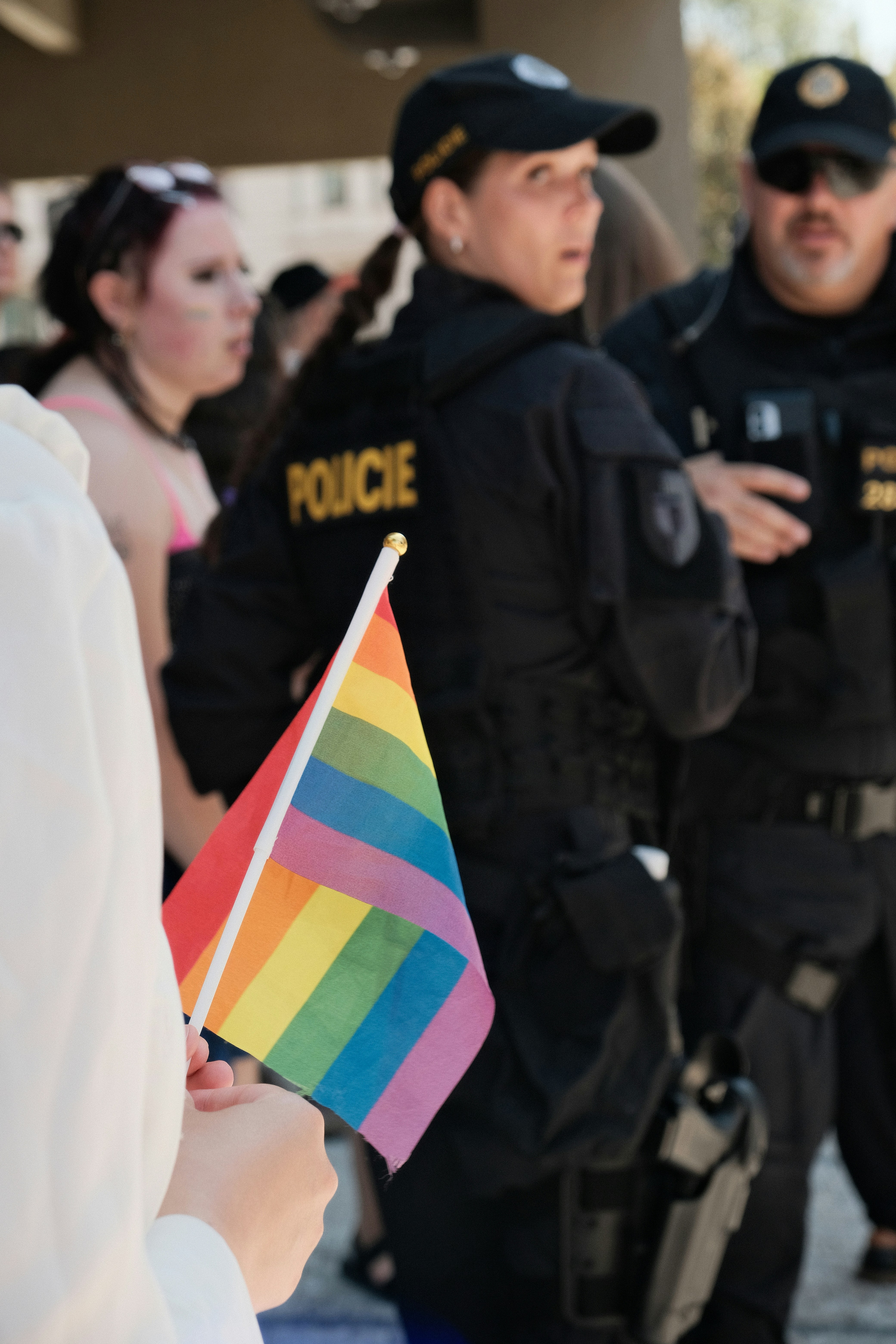 Eine Hand, die eine kleine Regenbogenflagge hält, mit Polizisten im Hintergrund.