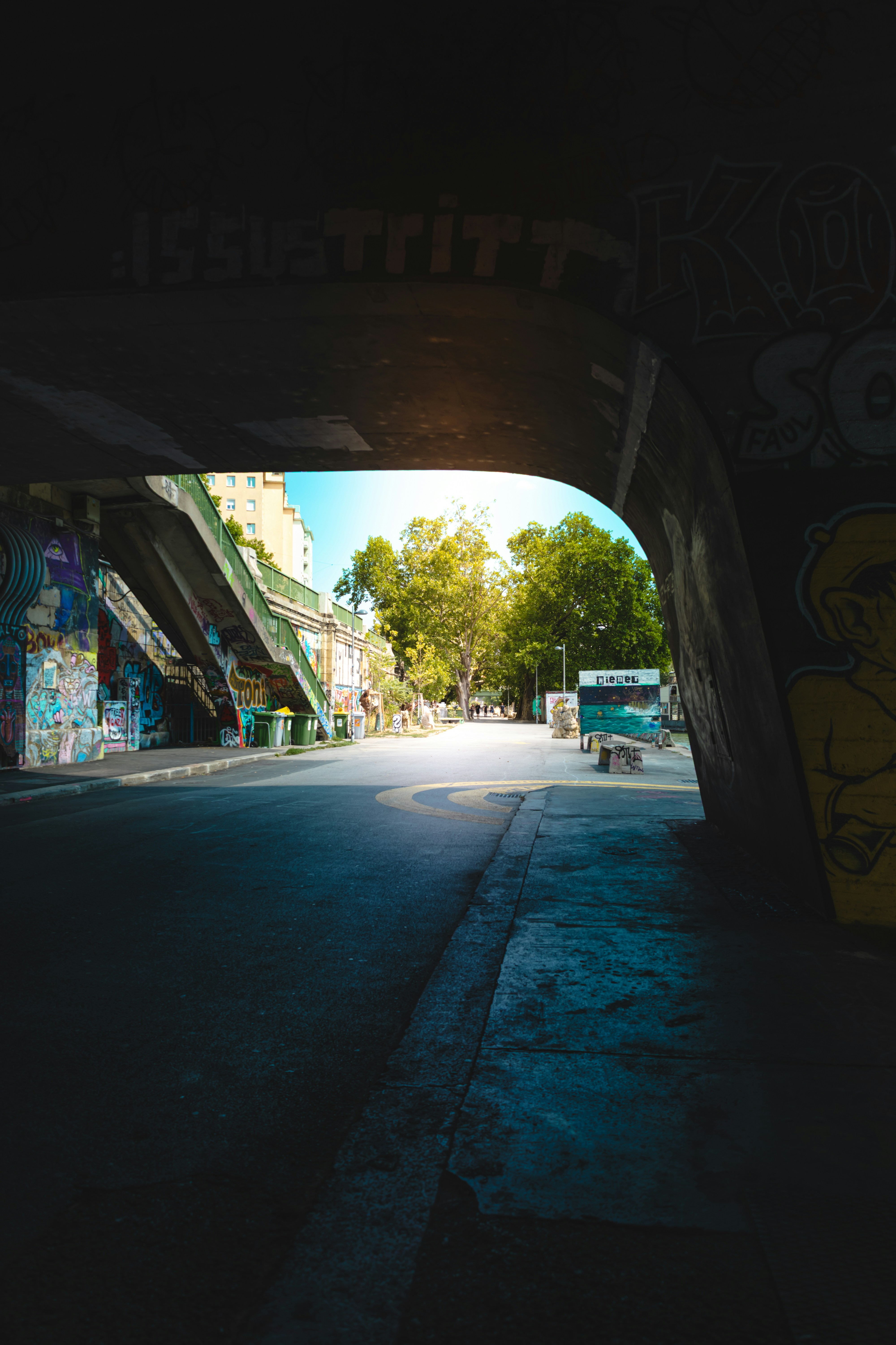 Ein Blick durch einen mit Graffiti bedeckten Betontunnel auf eine sonnenbeschienene Straße mit Bäumen