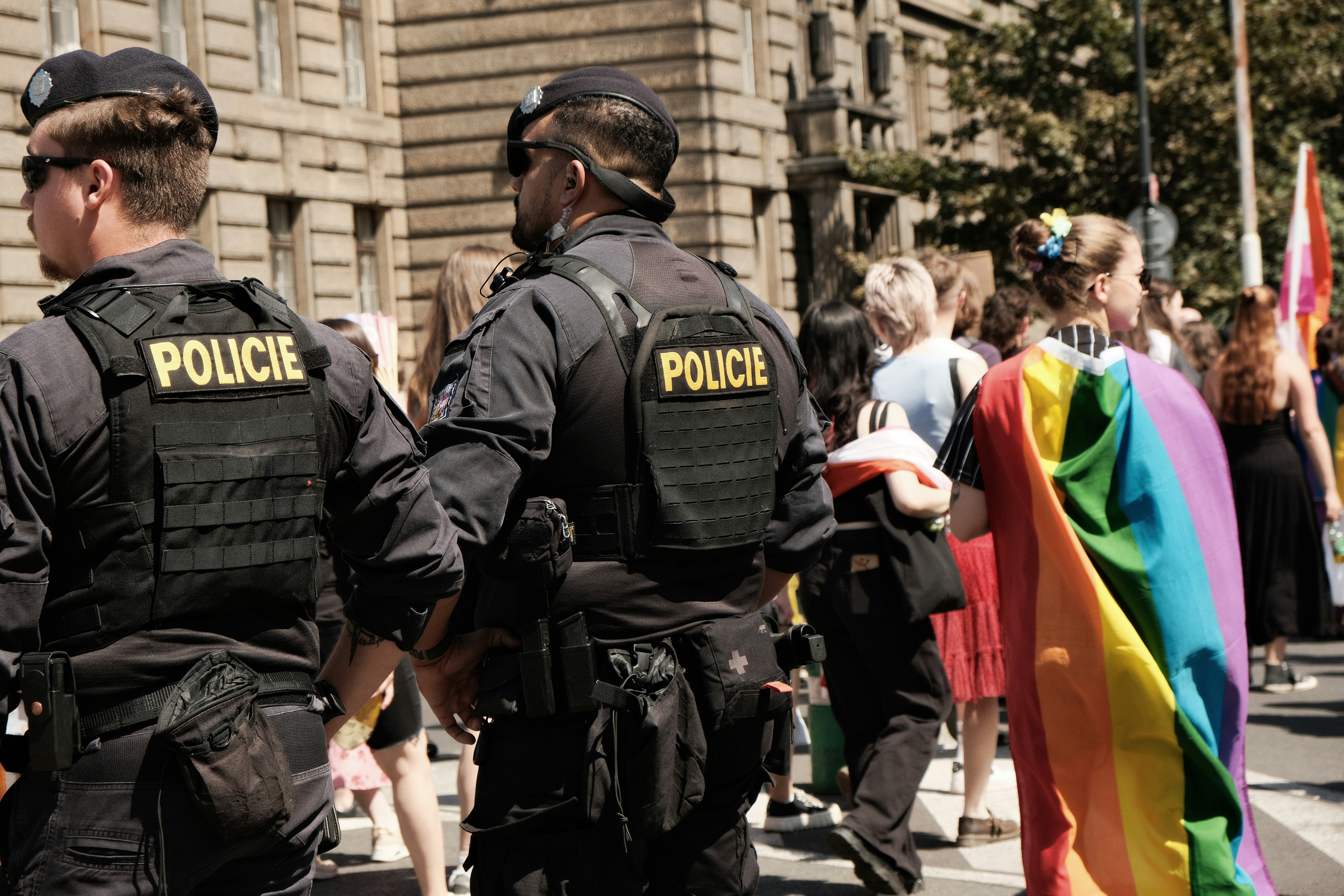 Zwei Polizisten in schwarzen Uniformen überwachen eine Pride-Parade auf einer Stadtstraße.