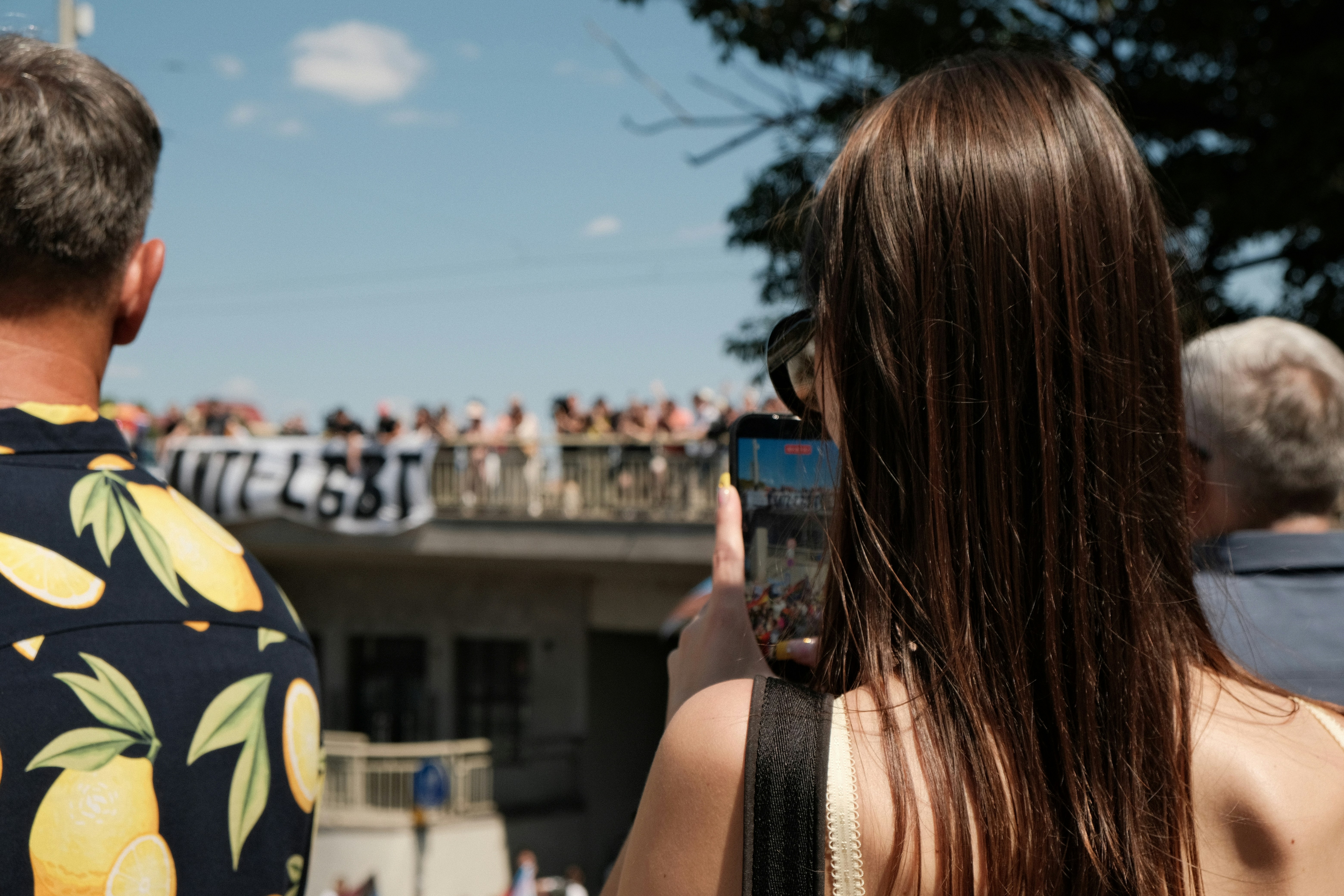 Eine Frau, die mit ihrem Smartphone eine Menschenmenge auf einer Brücke filmt.