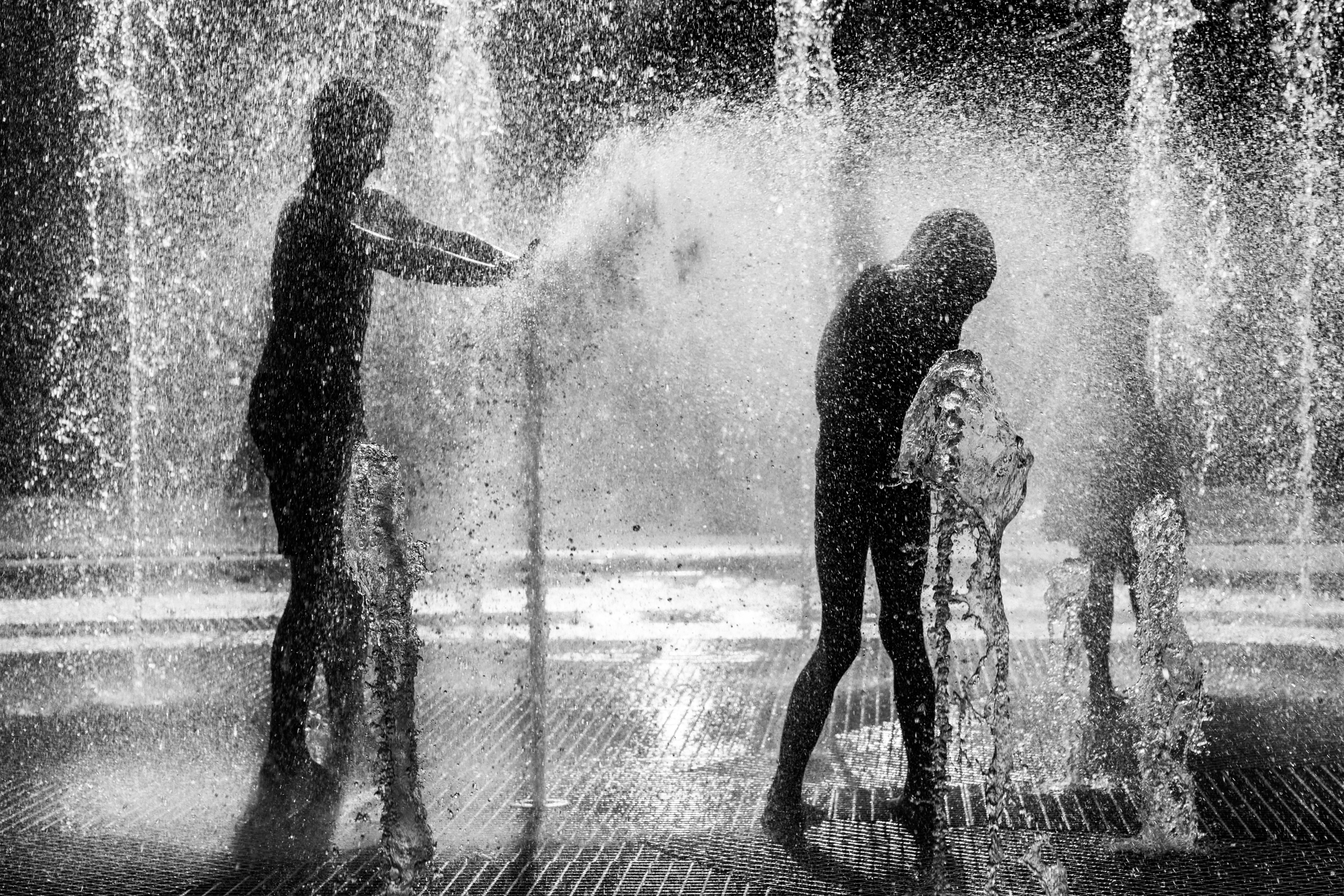 Deux personnes jouant dans le jet d’une fontaine publique en noir et blanc