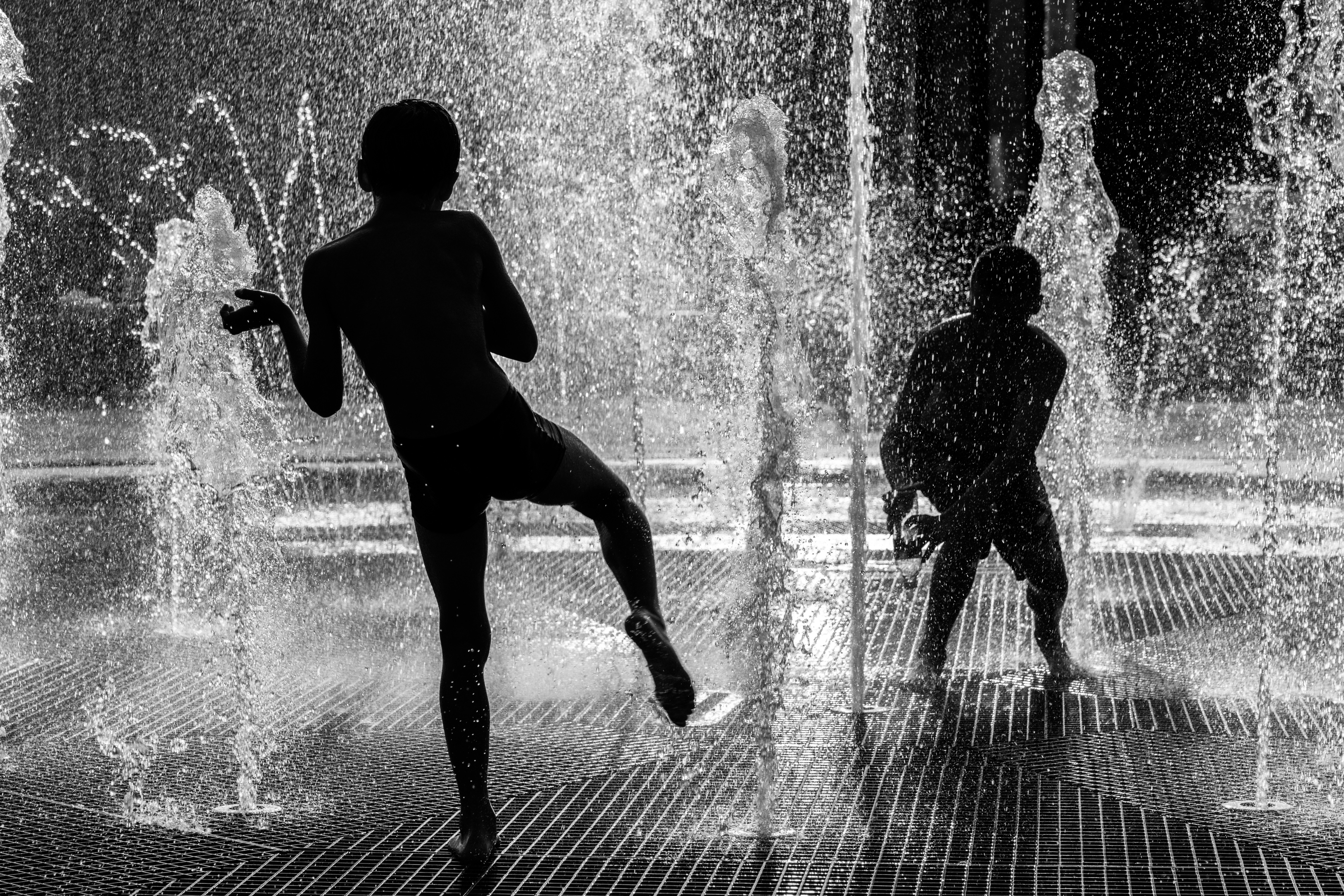 Deux personnes en silhouette jouant dans une fontaine avec des jets verticaux d’eau