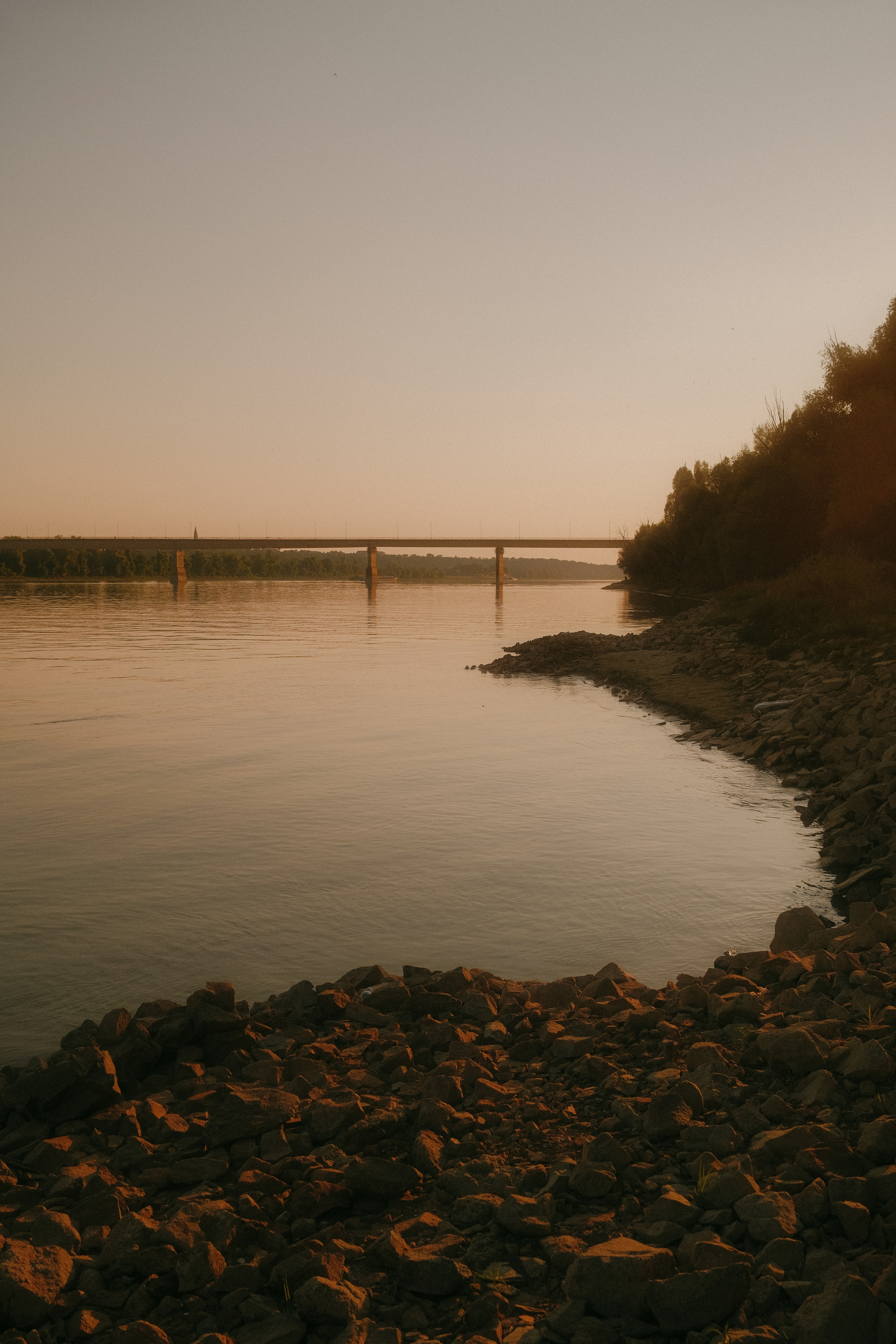 A bridge spanning a wide river under a warm golden sky.
