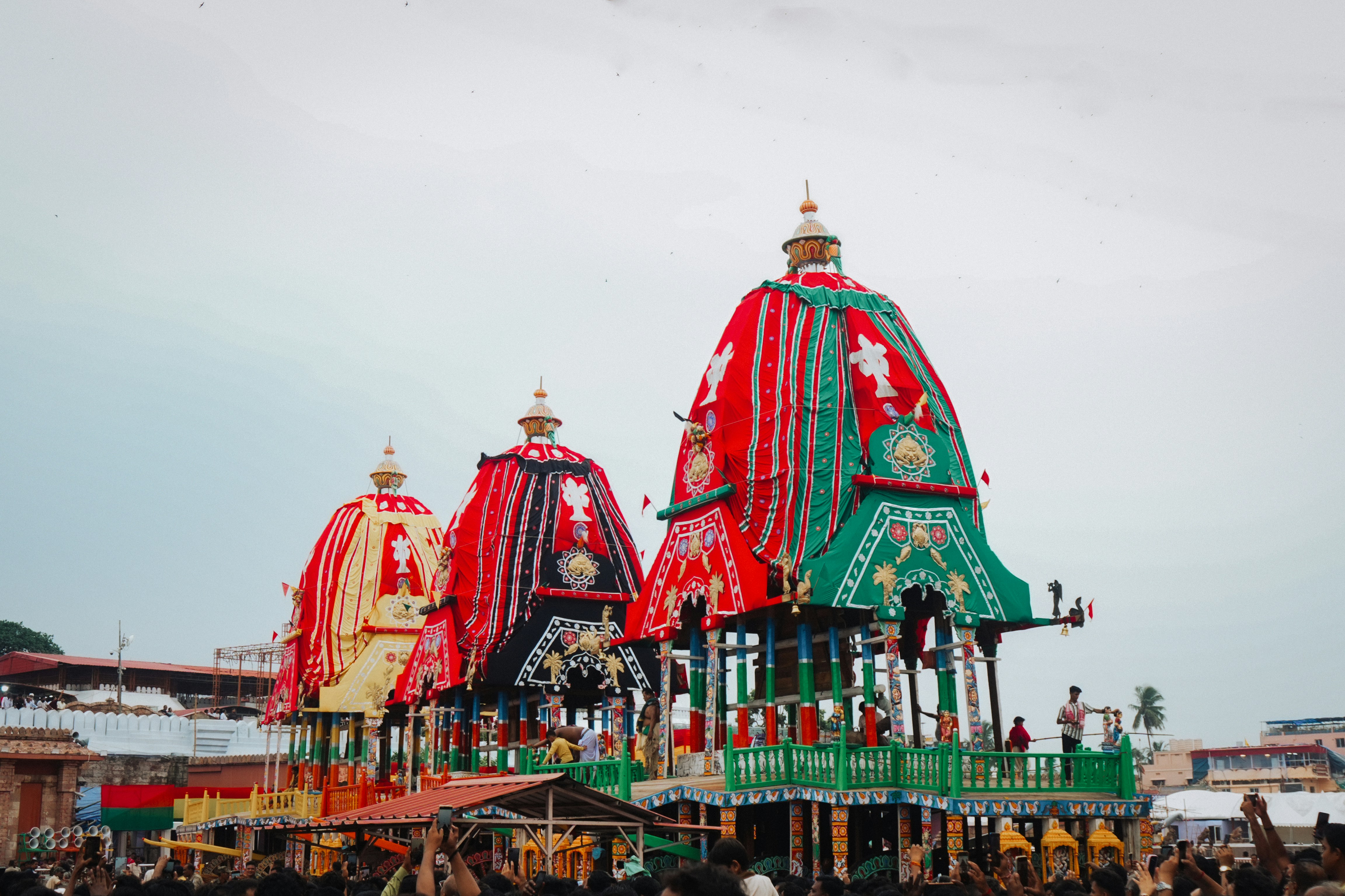 Three ornate wooden chariots decorated with red, green, and yellow fabric in Puri, India