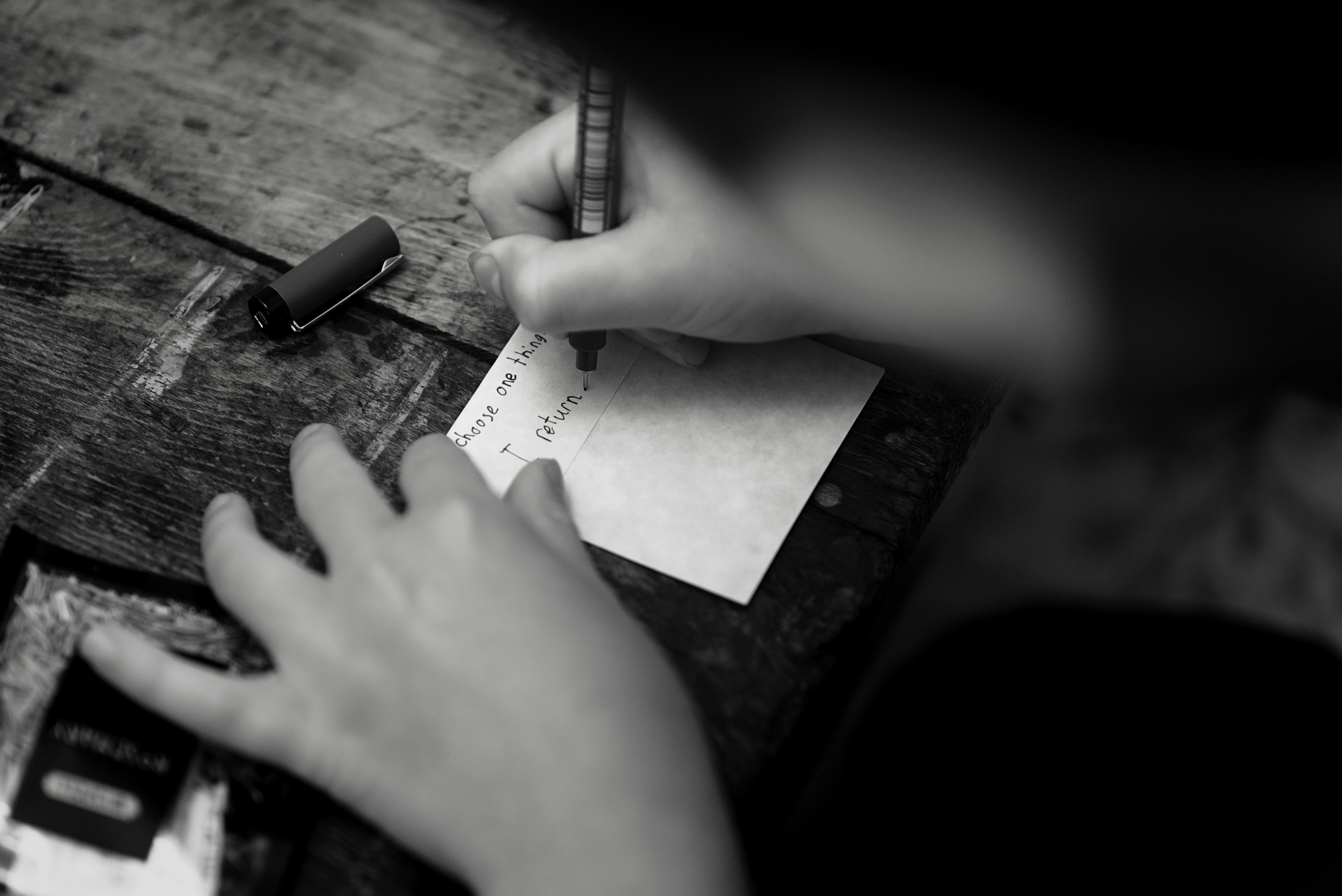 A person writing on a small card with a pen on a wooden table.