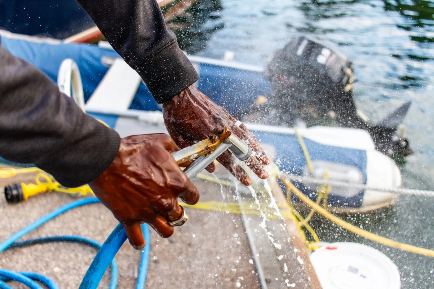 A person rinsing a small boat with a hose beside the water
