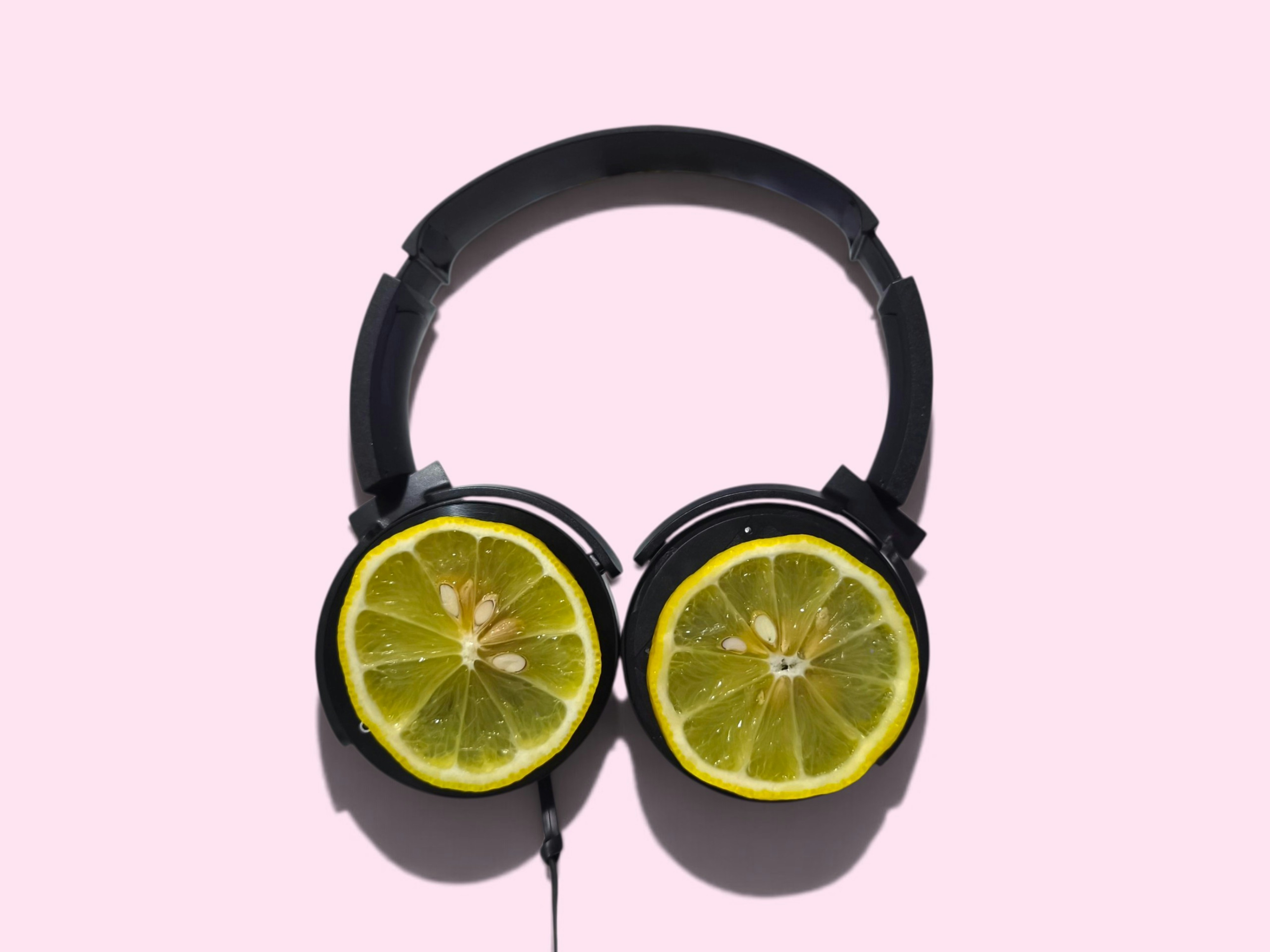 Black headphones with lemon slices over the ear cups on a pink background