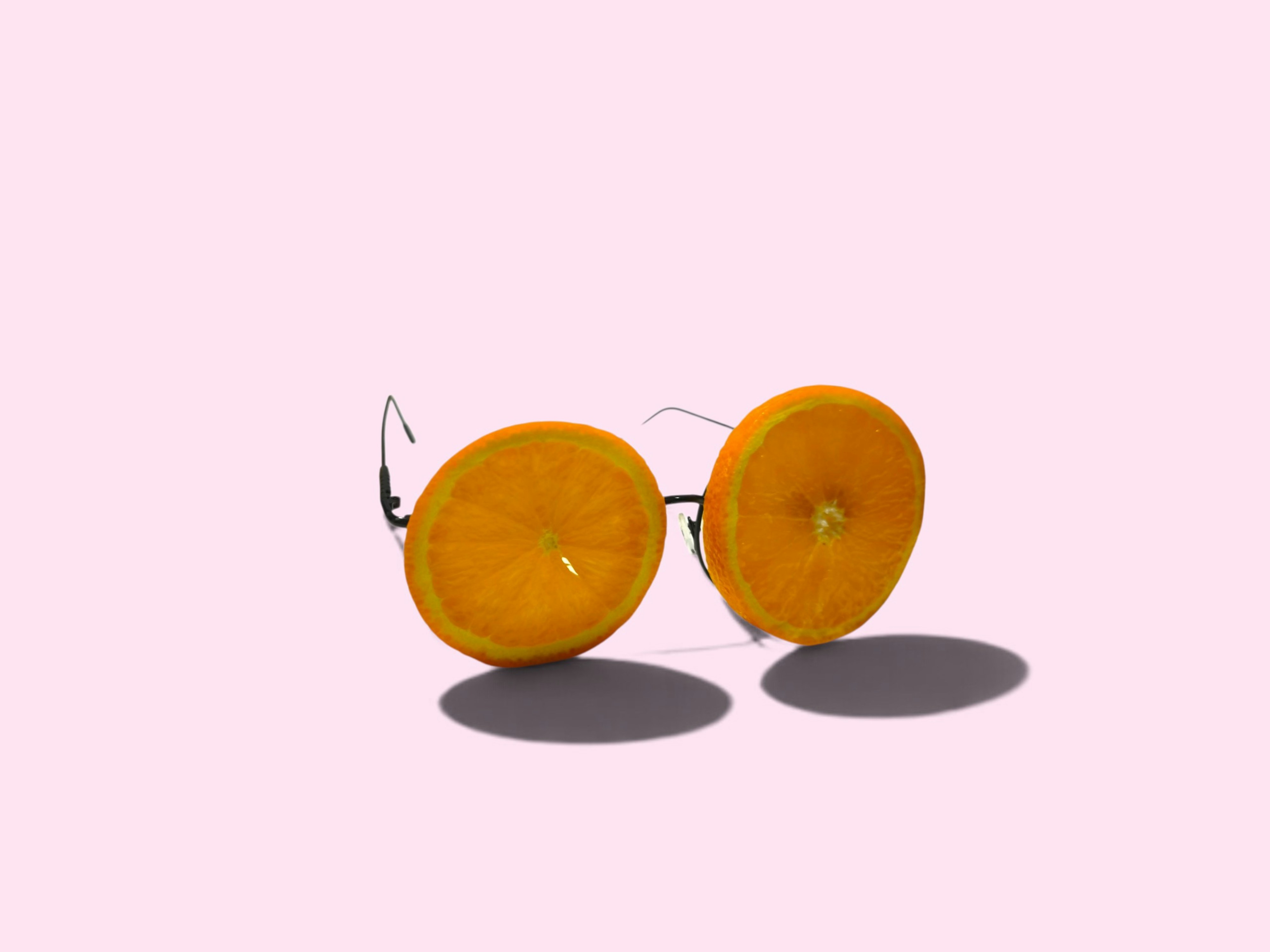 A pair of glasses with orange slices as lenses on a pink background