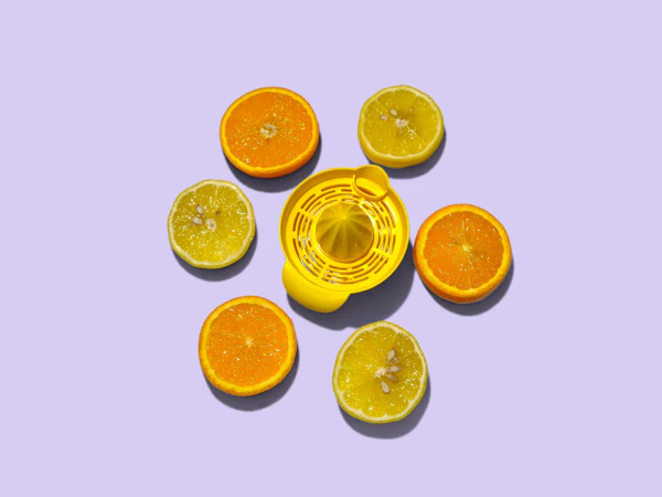 A yellow citrus juicer with oranges and lemons on a purple surface