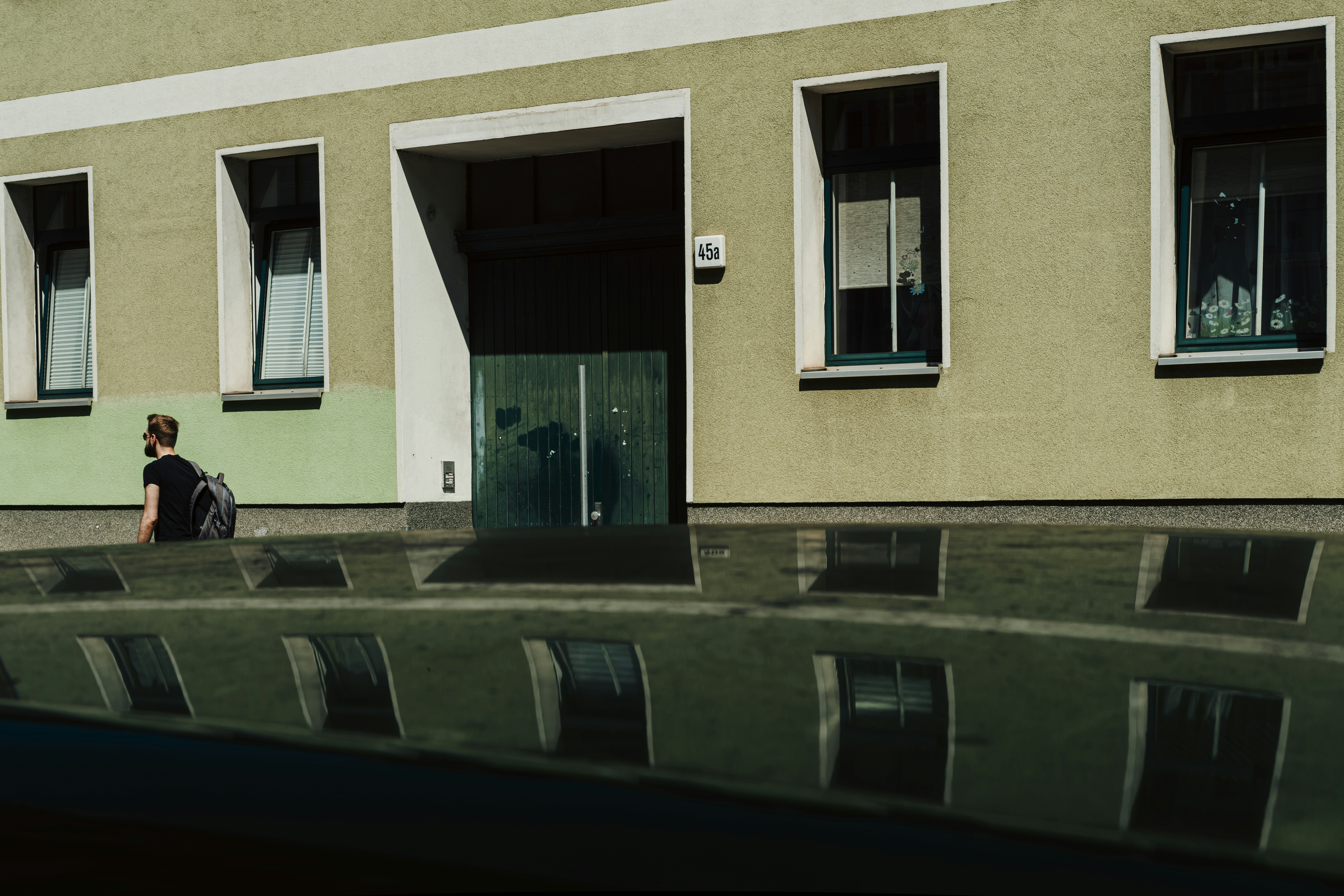 A person with a backpack walking past a green building in Brandenburg, Germany.