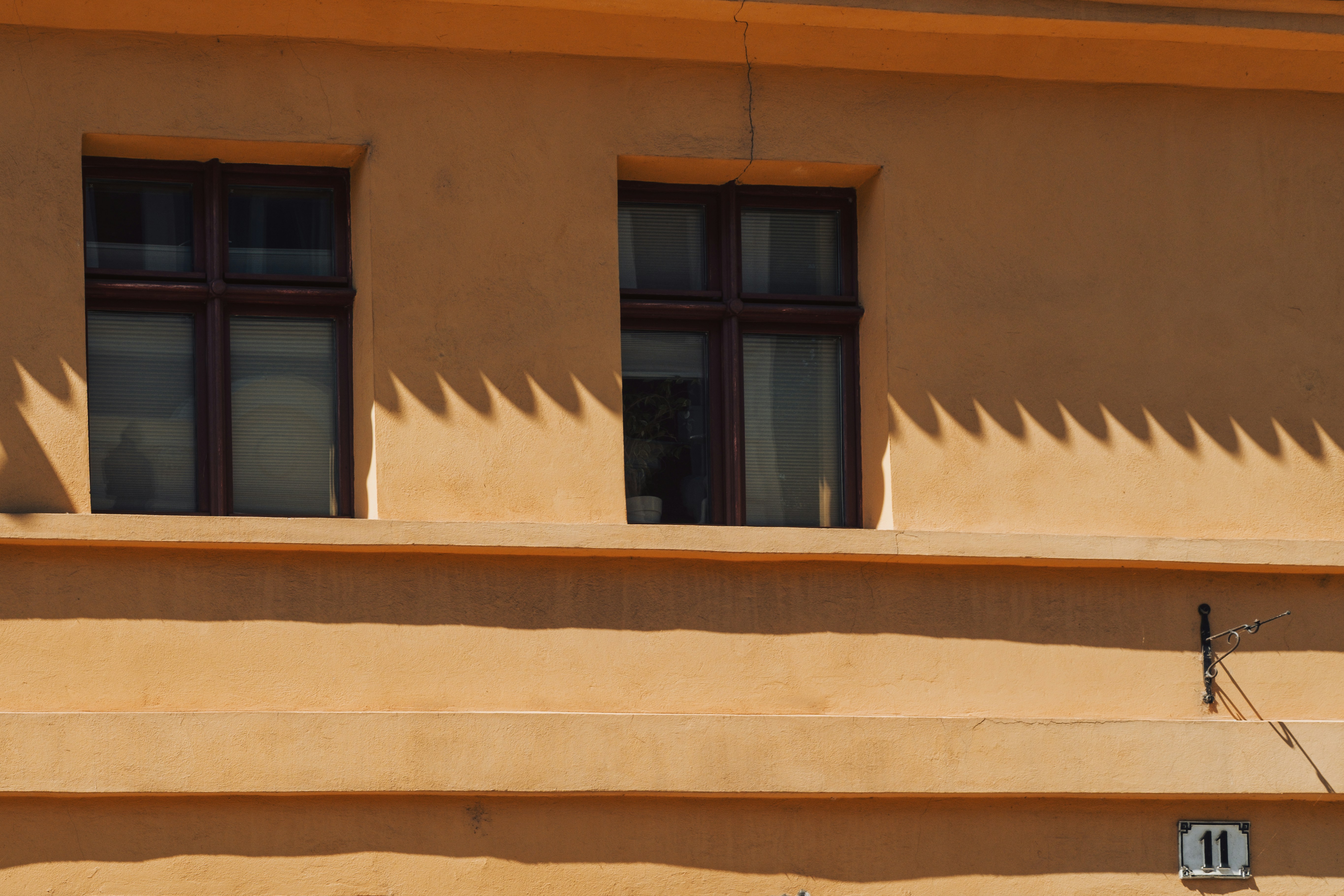 Two windows on an orange building facade with a jagged shadow in Brandenburg.