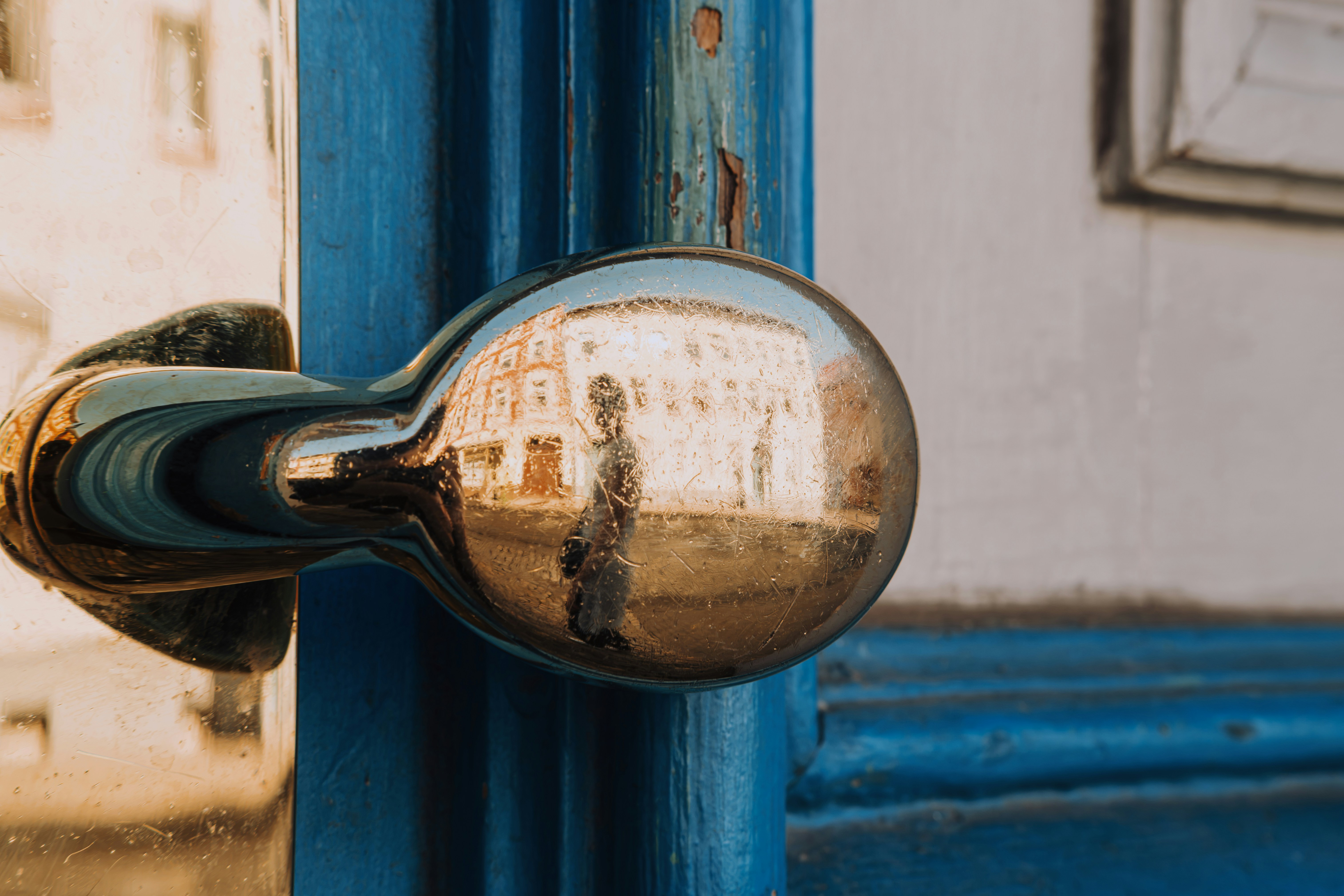 A person reflected in a polished metal door handle on a blue door.