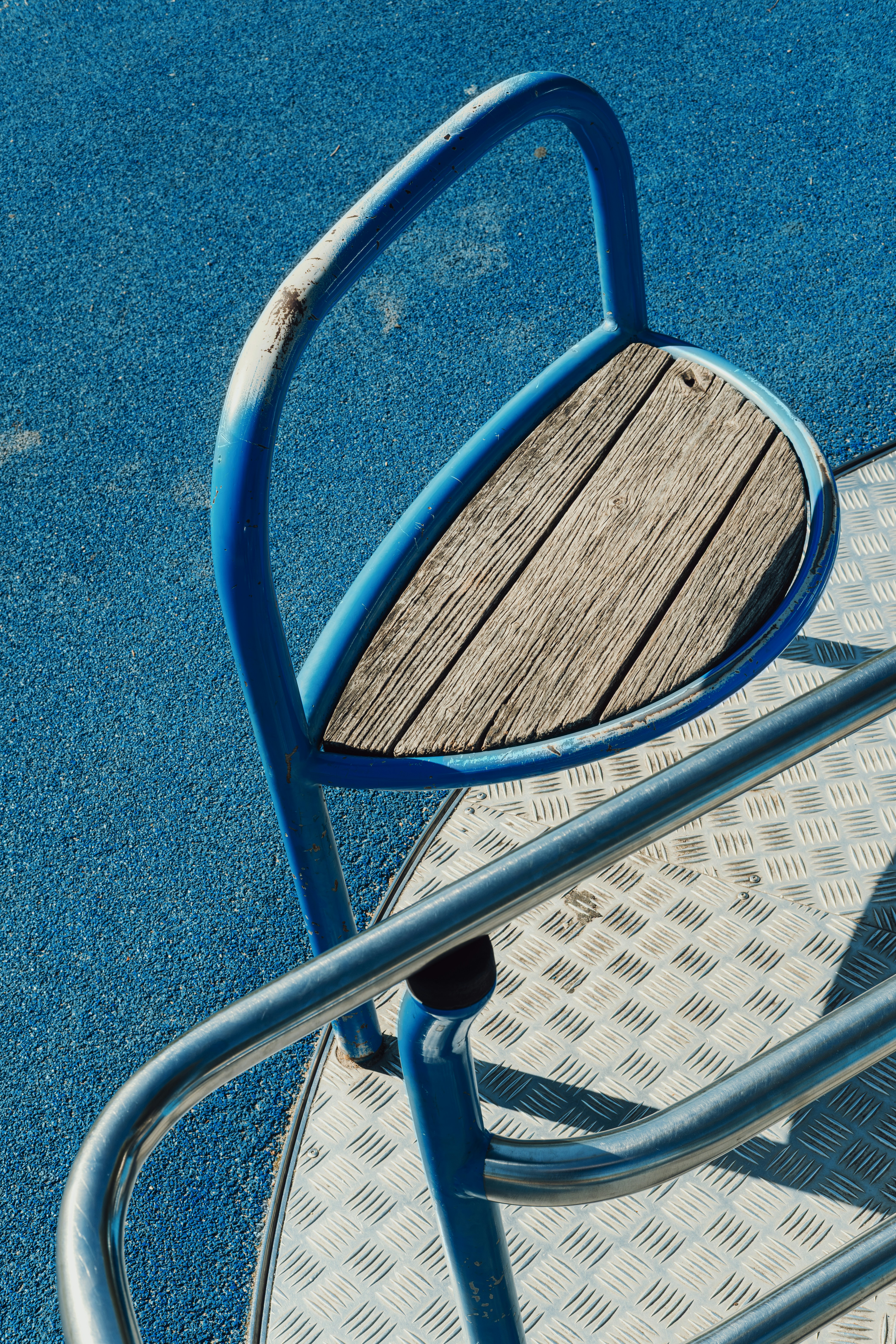 A blue metal merry-go-round seat with wooden slats on a blue rubber surface.