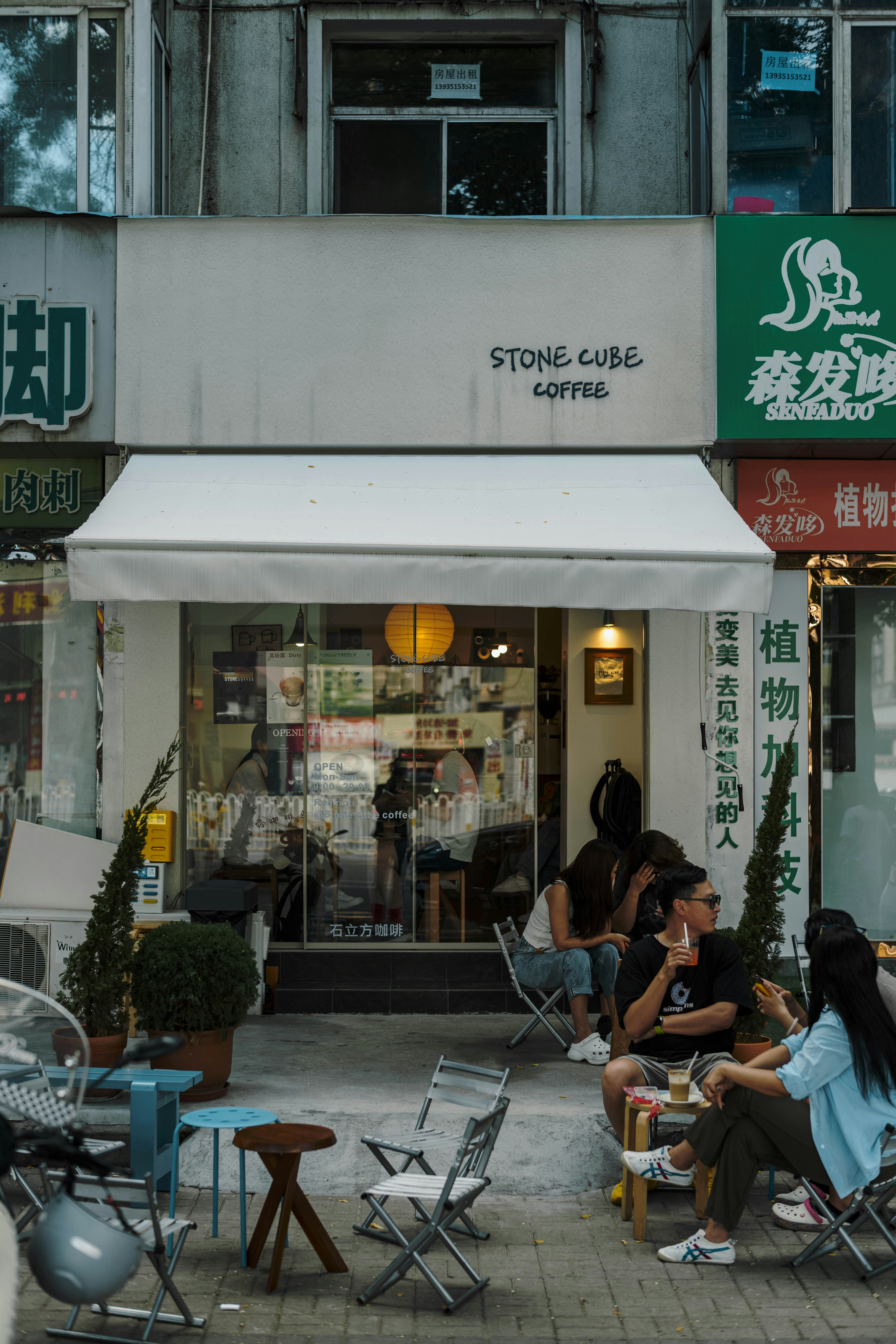 하얀 차양이 있는 커피숍 밖 테이블에 앉아 있는 사람들.