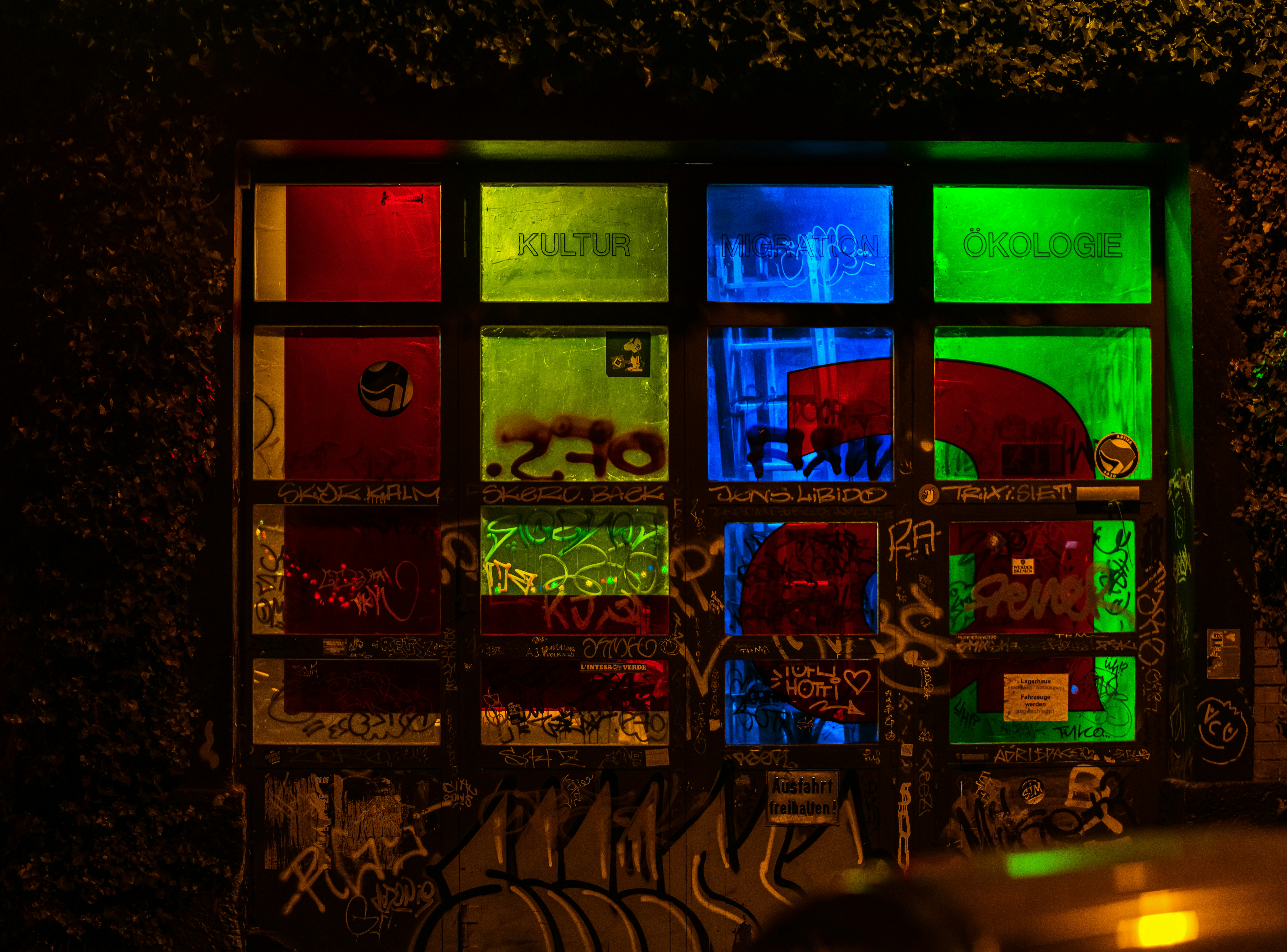 A grid of windows illuminated in red, green, and blue with graffiti and stickers