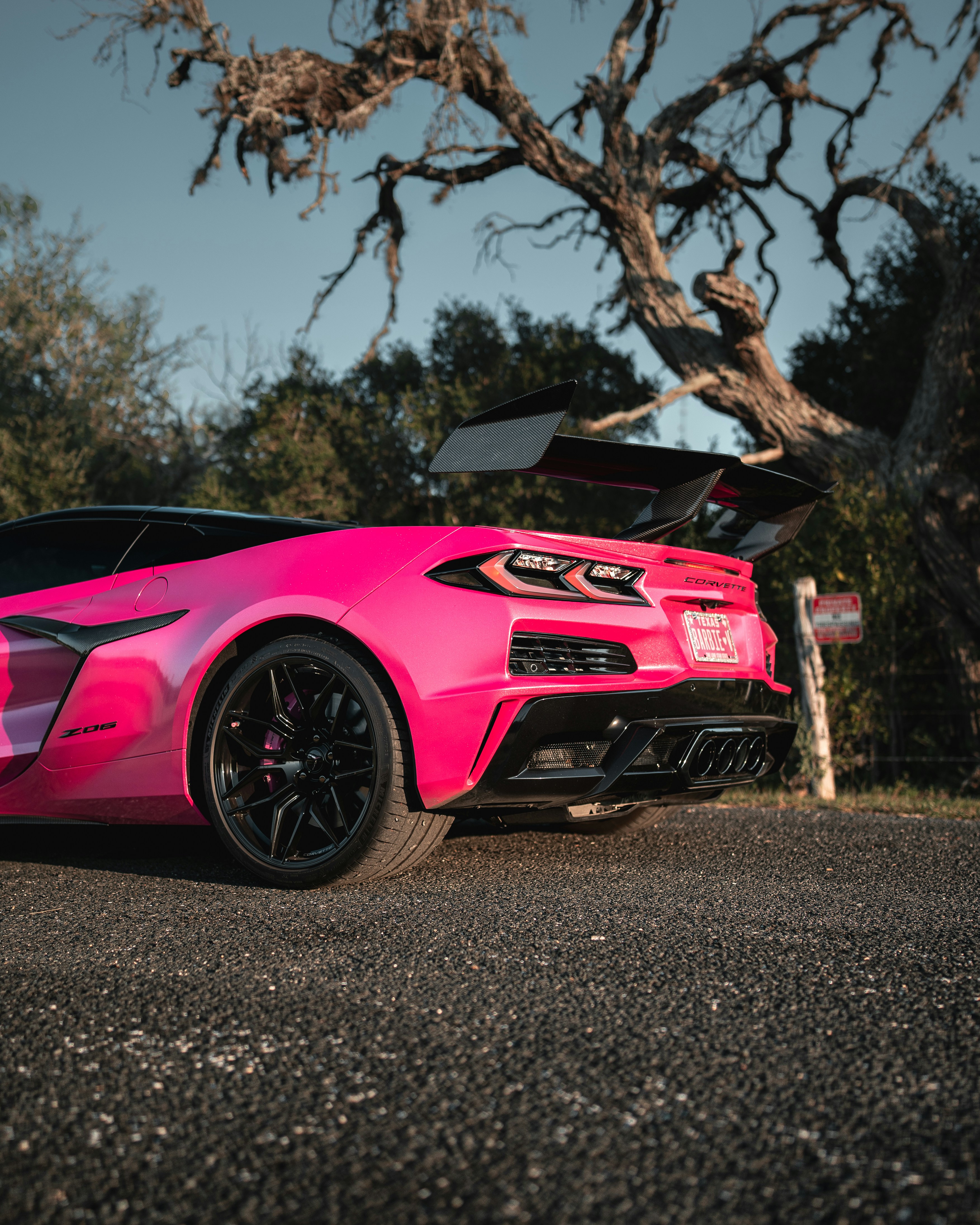 明るいピンクのシボレー・コルベットZ06で、アスファルトの上に大きなリアウイングが付いています