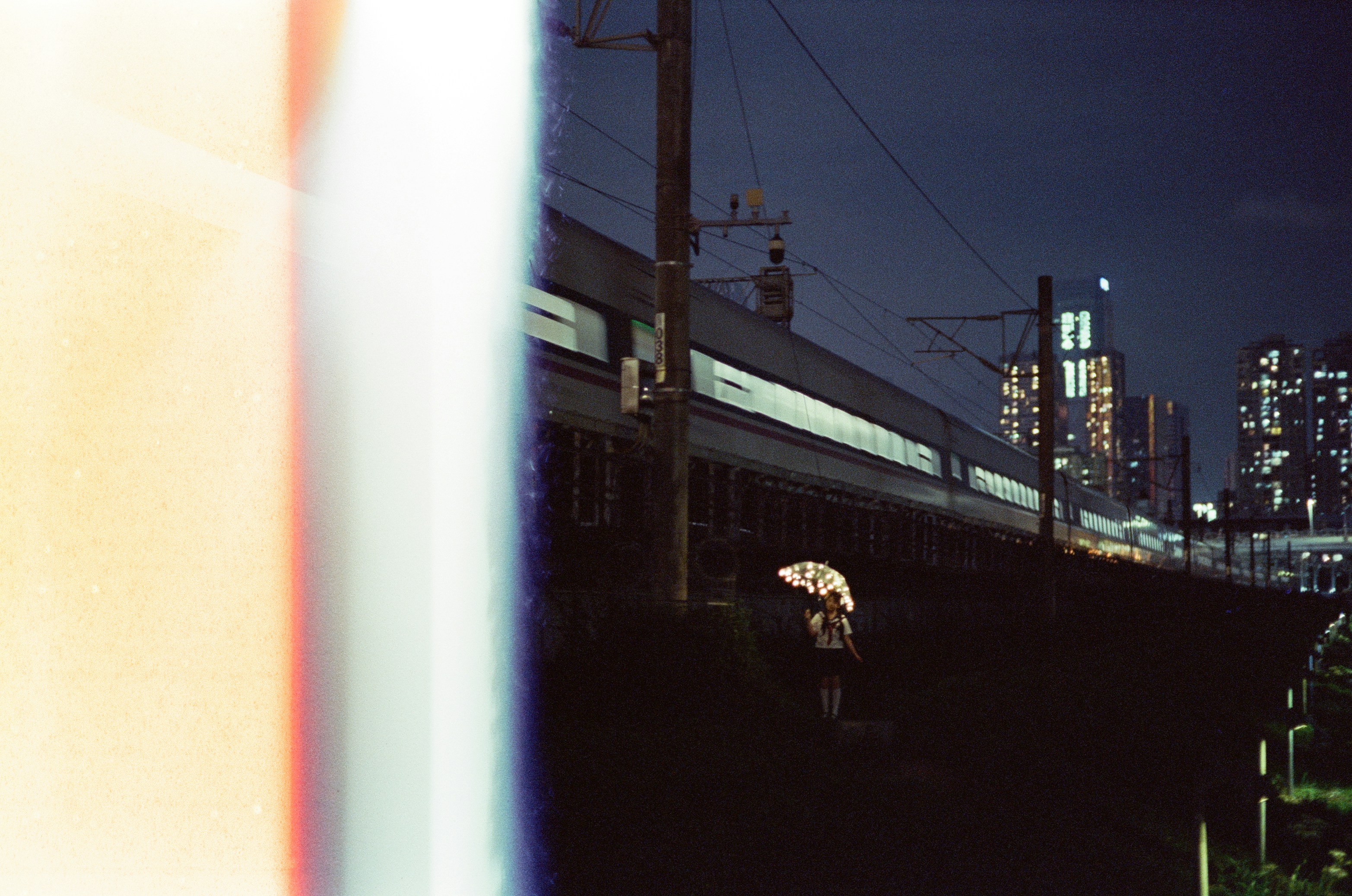 A person holding a glowing umbrella near a passing train at night.