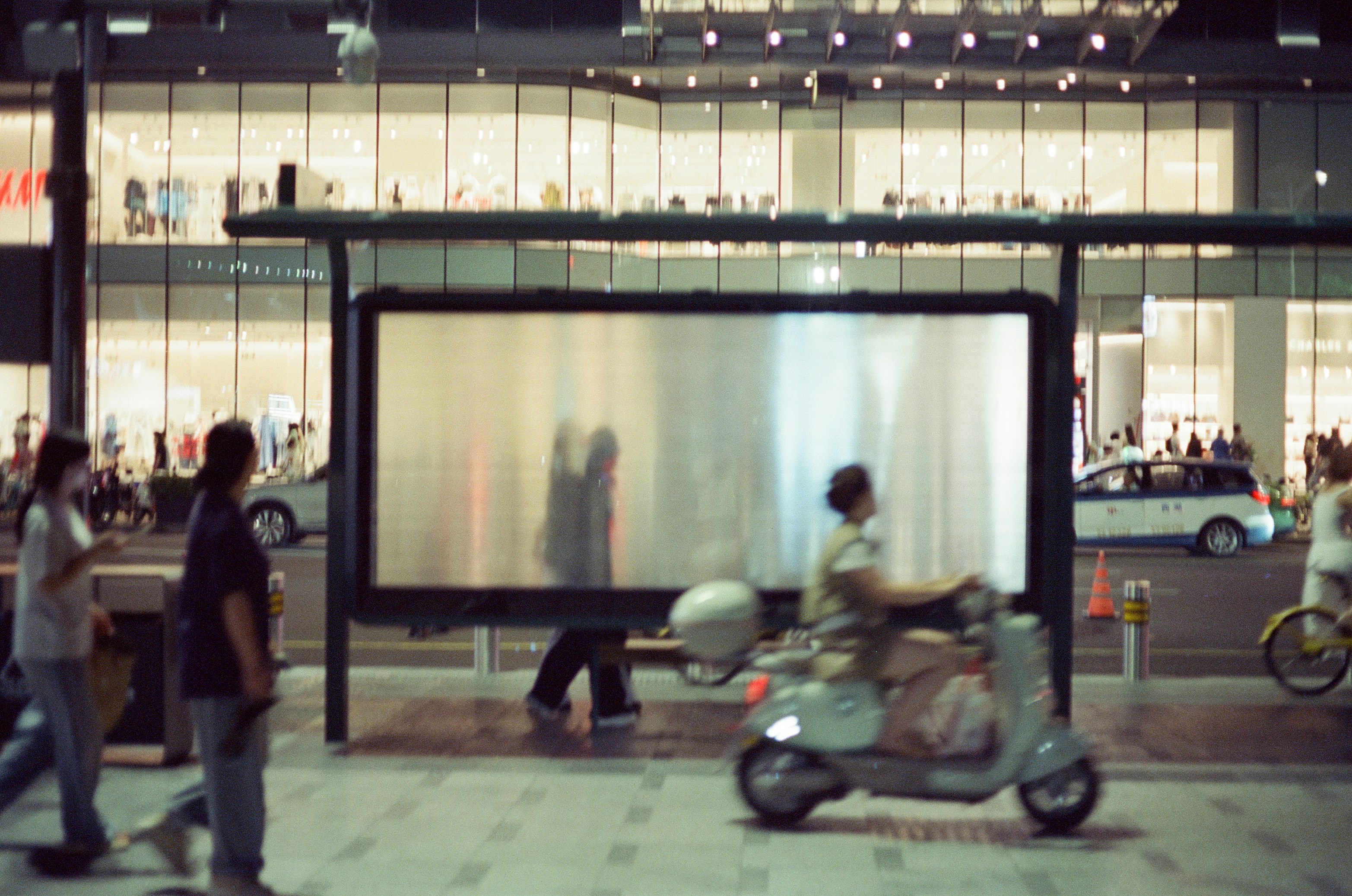 A person riding a scooter past a bus stop with a large blank billboard.