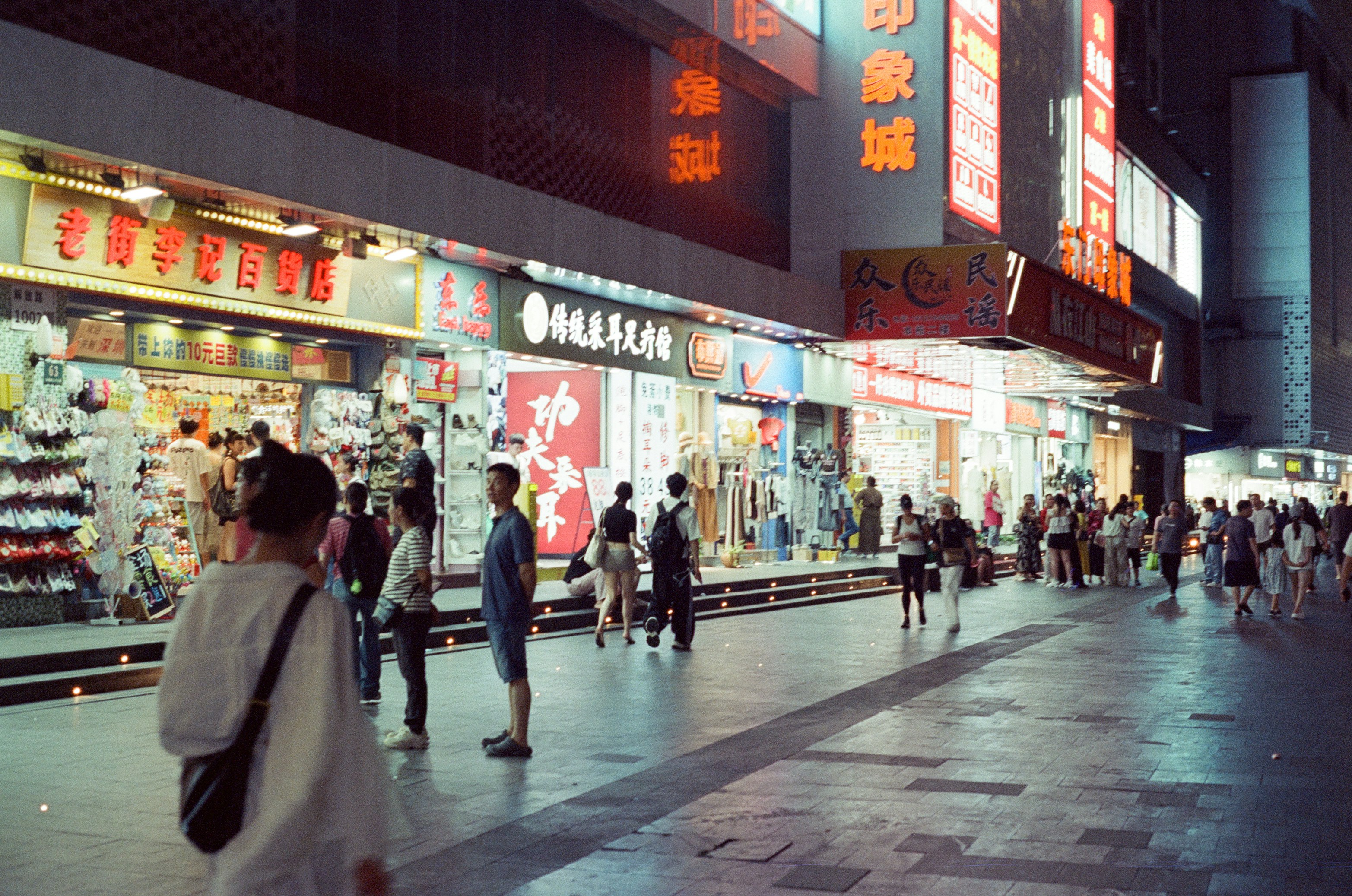 People walking along a brightly lit pedestrian street lined with shops at night.