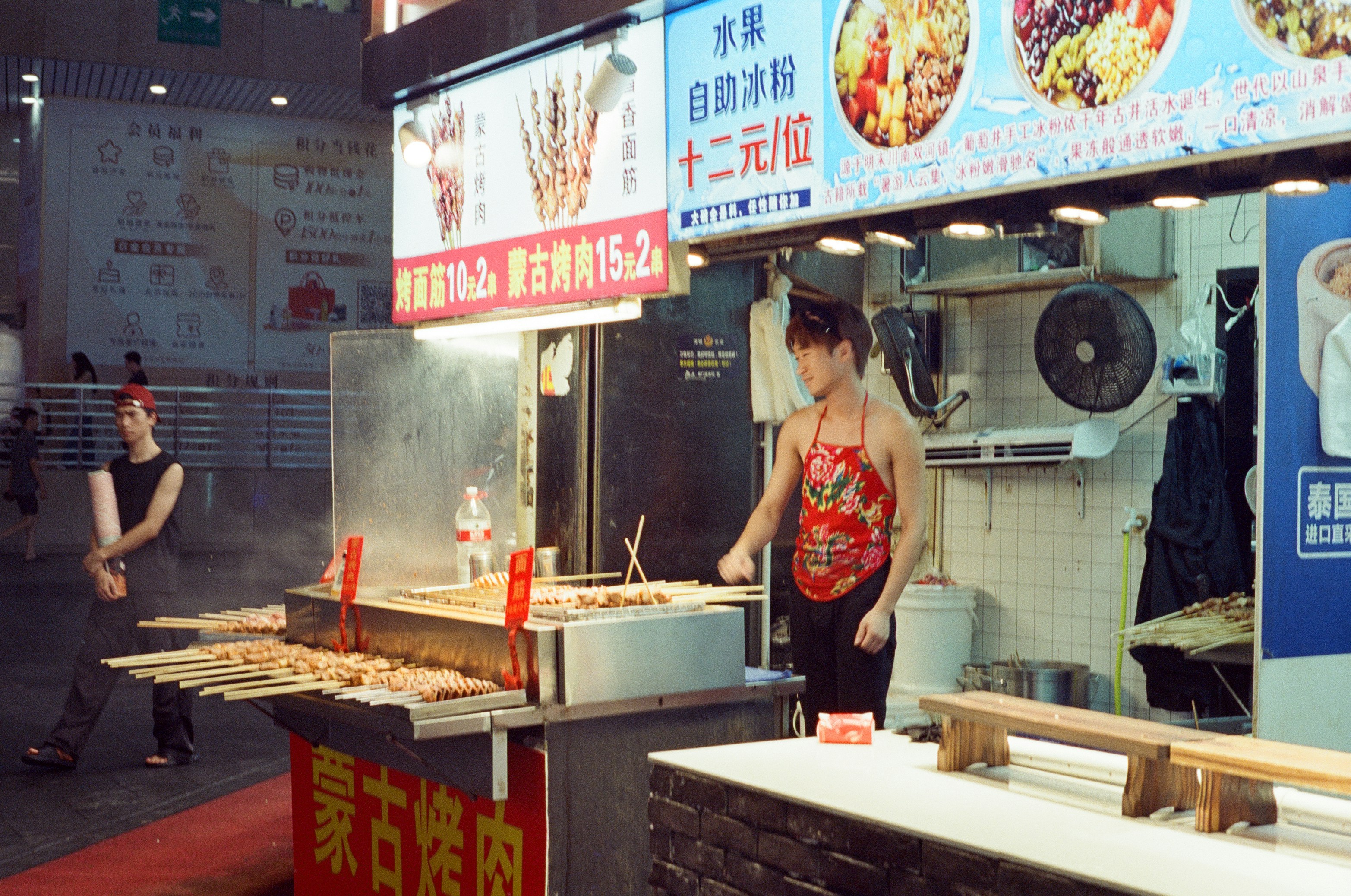A man in a red floral apron grilling meat skewers at a street food stall