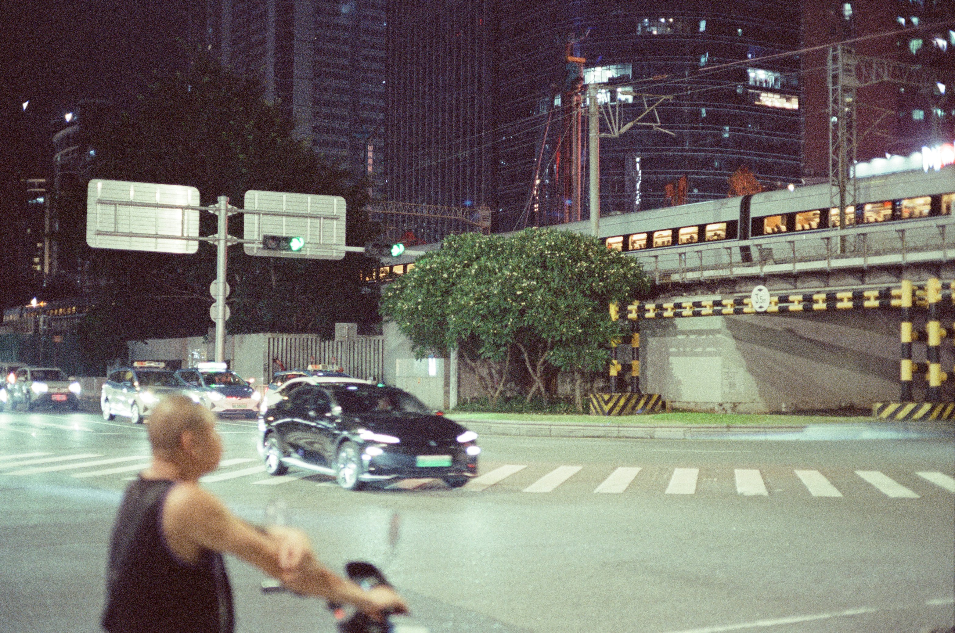 A person on a scooter at a city intersection with cars and a train.