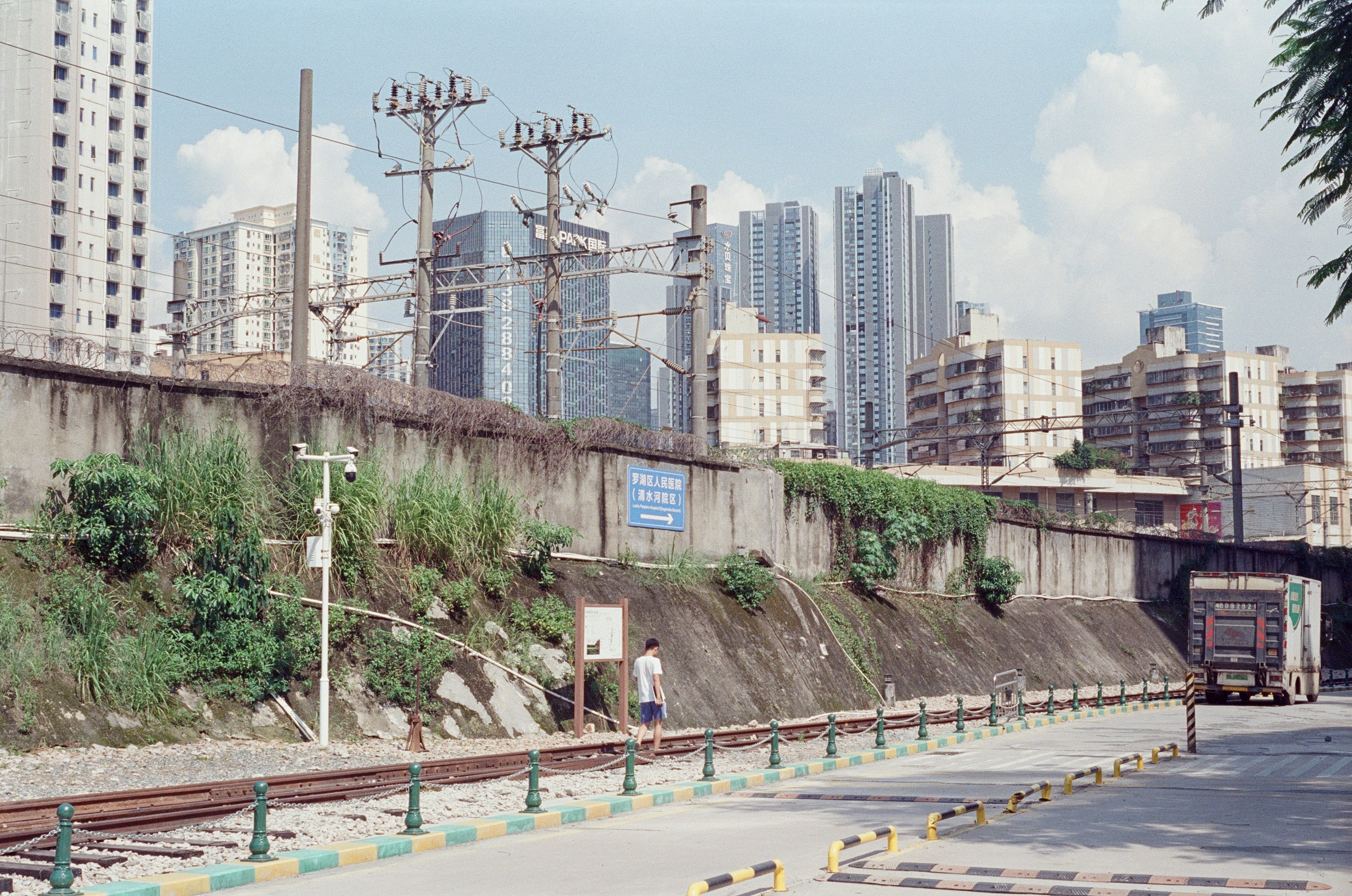 A person walking along railway tracks beside a concrete retaining wall in a city.