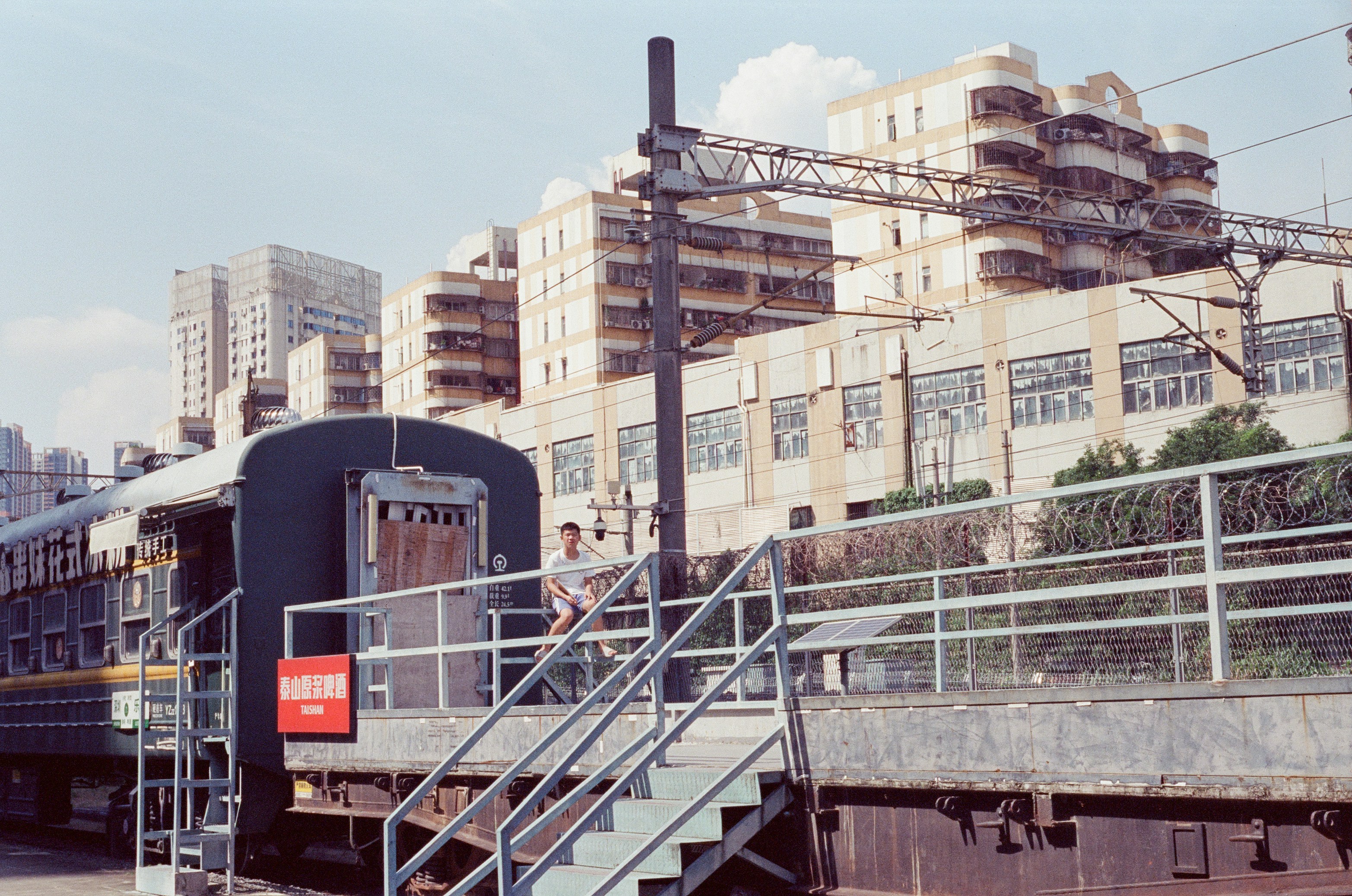 A person sitting on a metal staircase beside a train at a station.