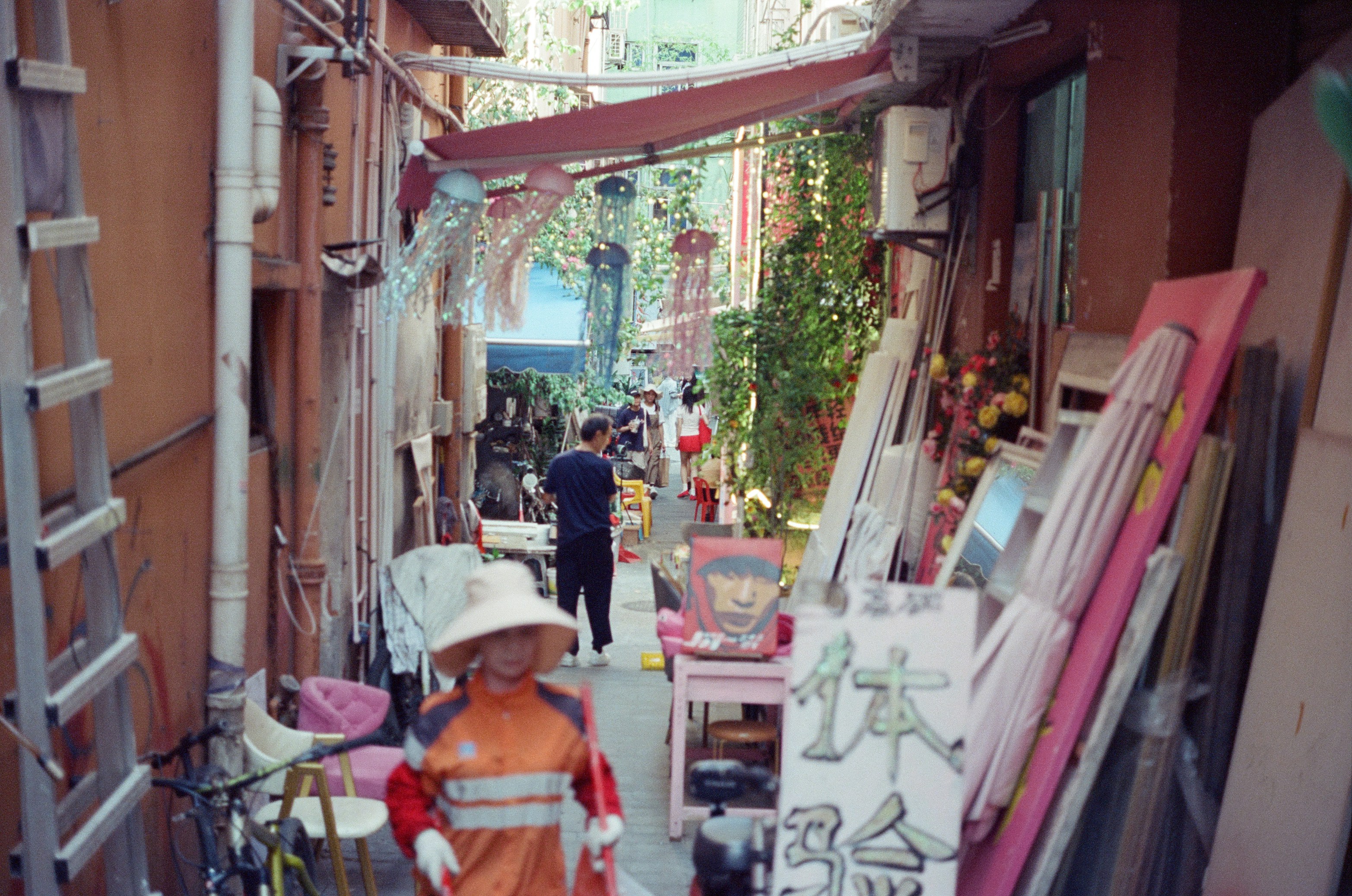 A person in an orange uniform walking through a narrow, cluttered urban alleyway.