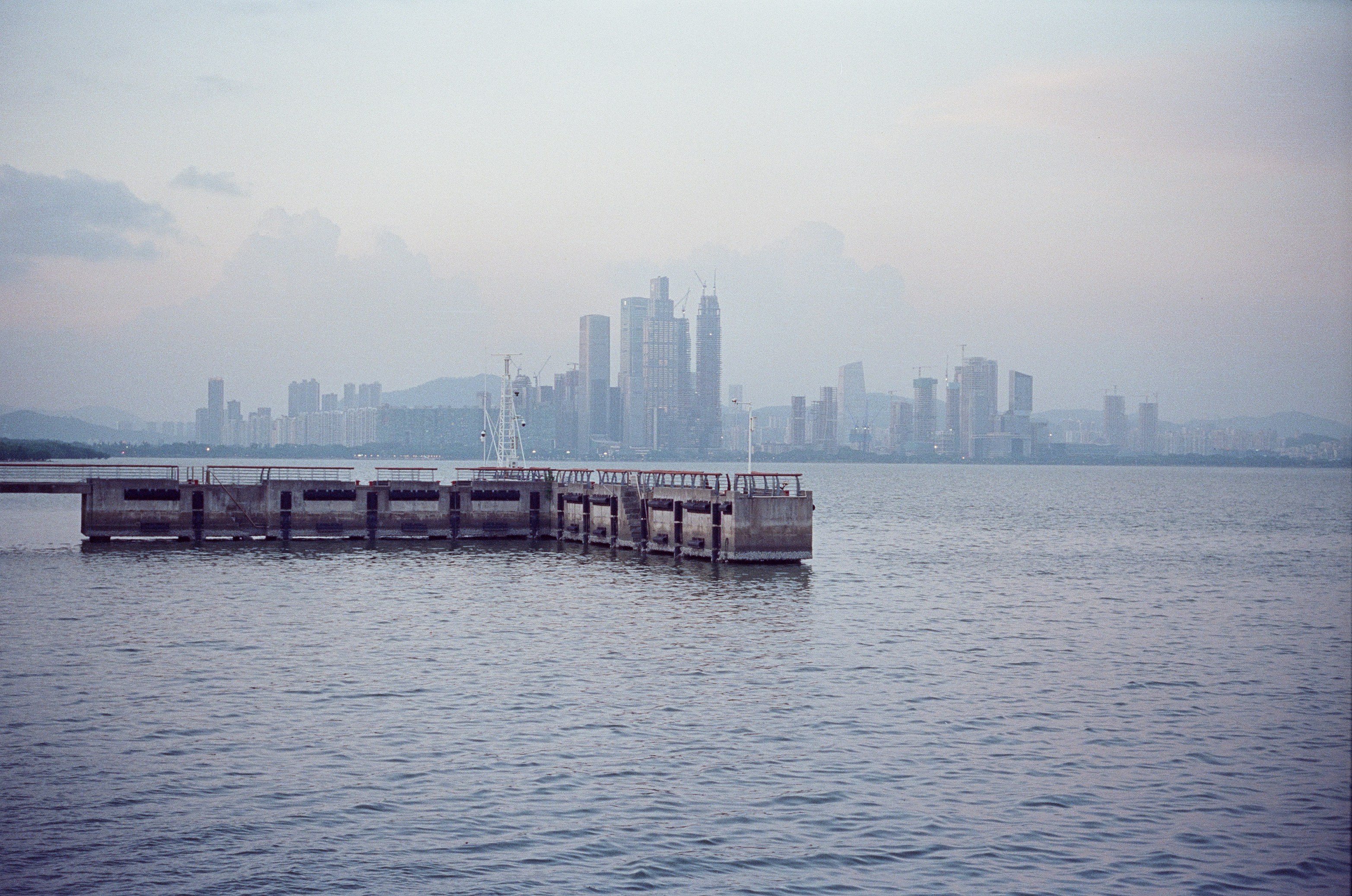 A concrete pier extending into calm water before a distant city skyline.