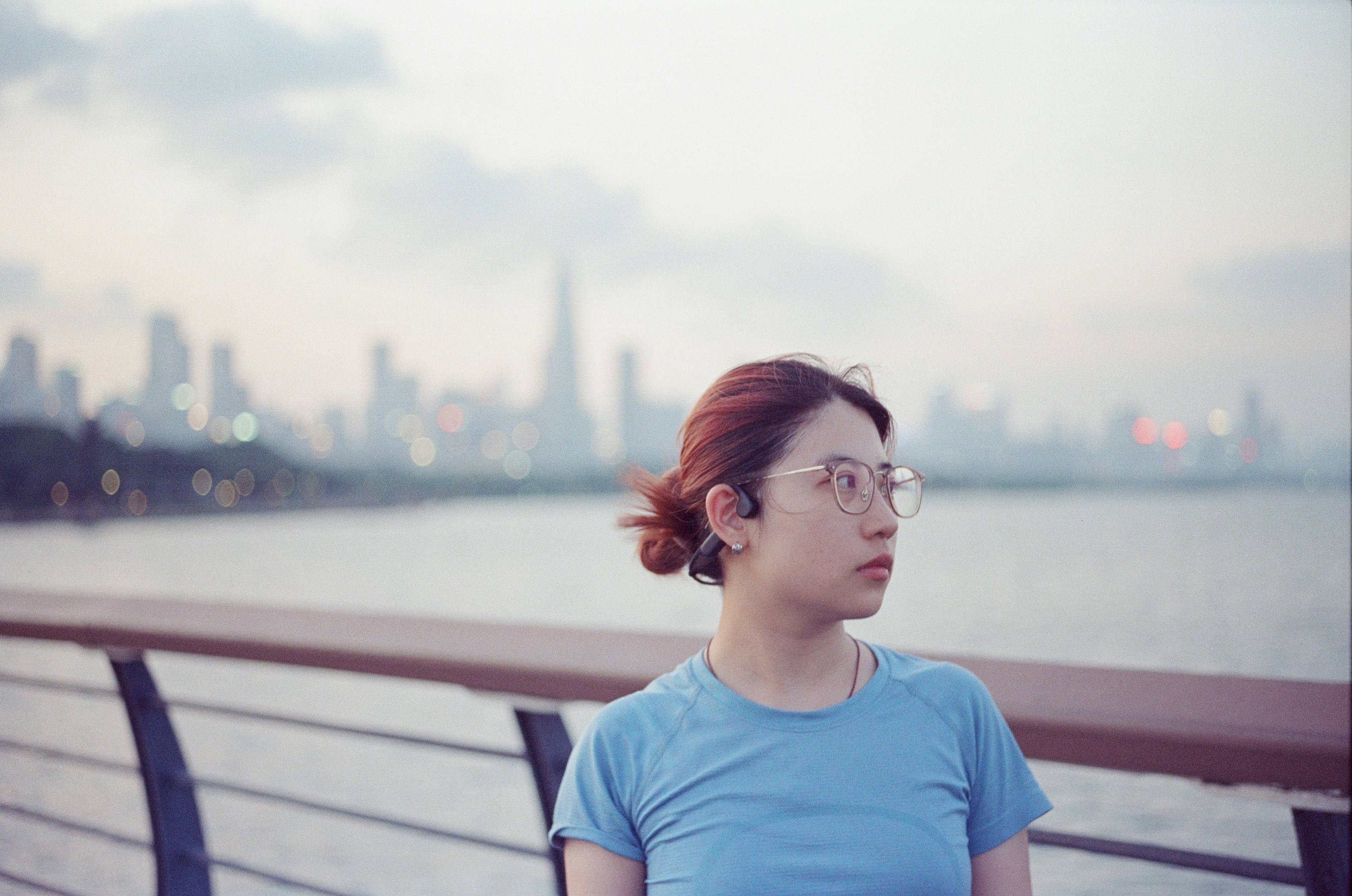 A woman with glasses and hair in a bun against a blurred city skyline.