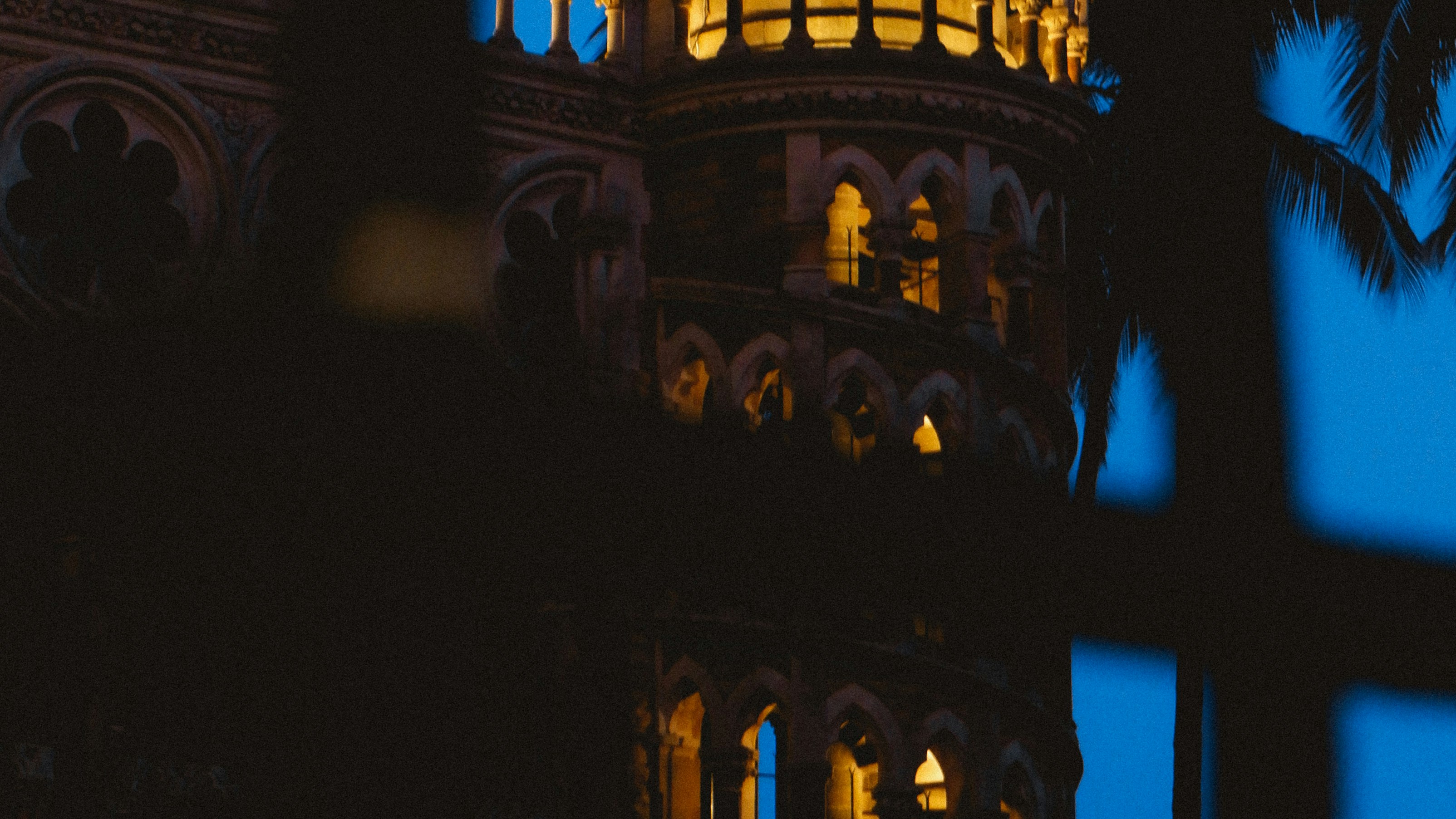 The illuminated arched windows of a historic stone tower at night.