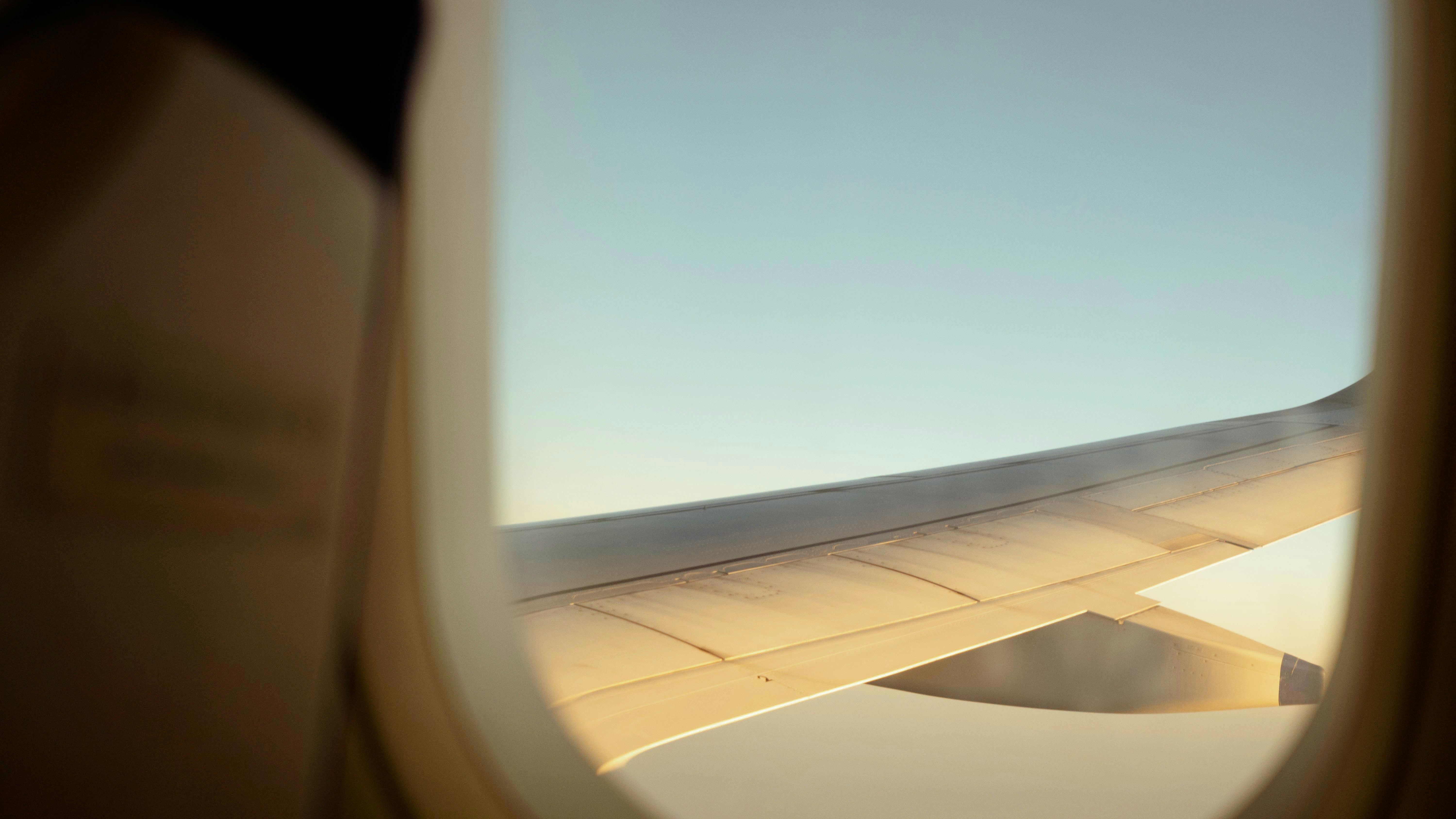 An airplane wing seen through a window against a clear blue sky.