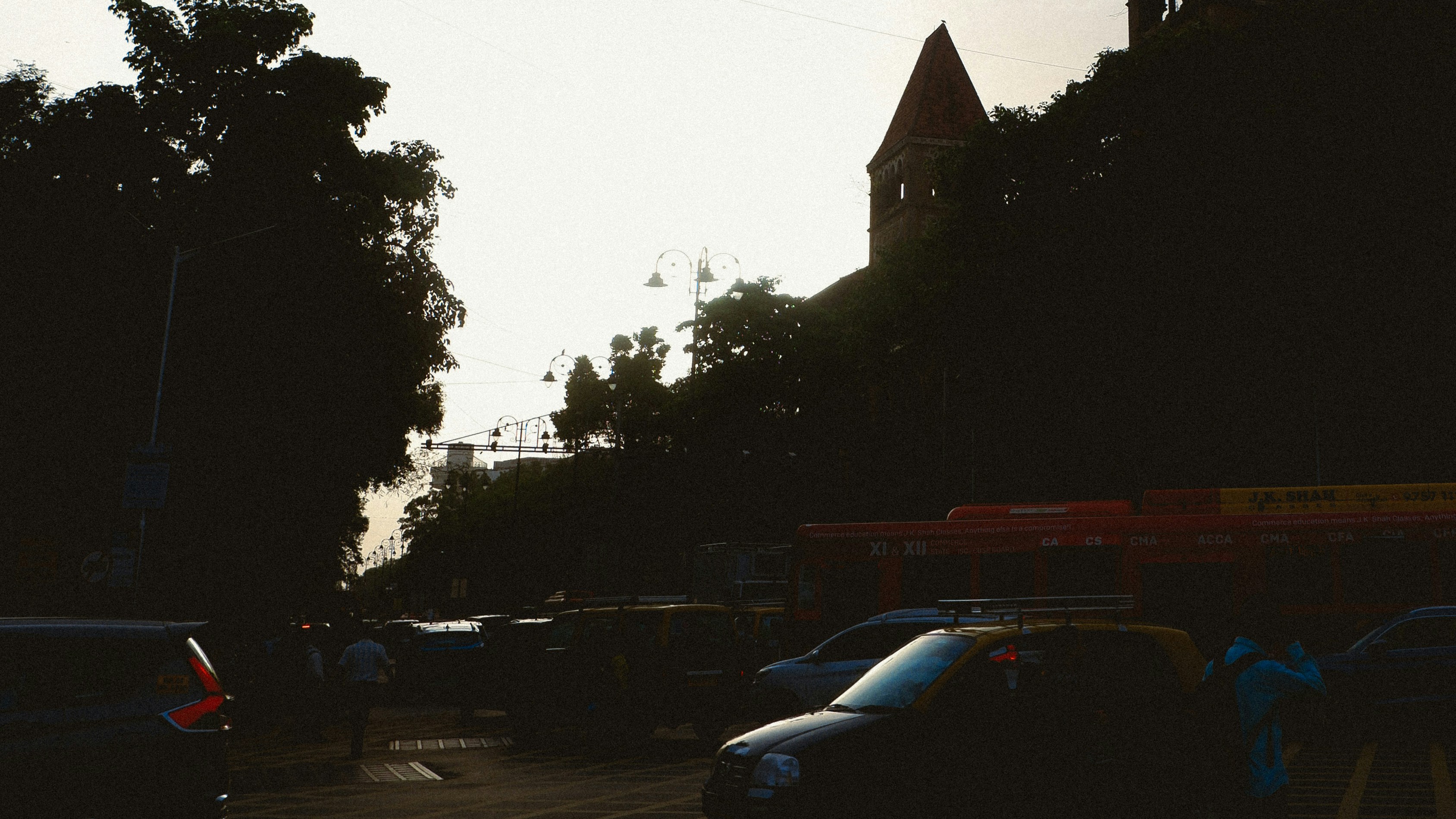 Traffic on a city street with a tall building silhouette against a bright sky.