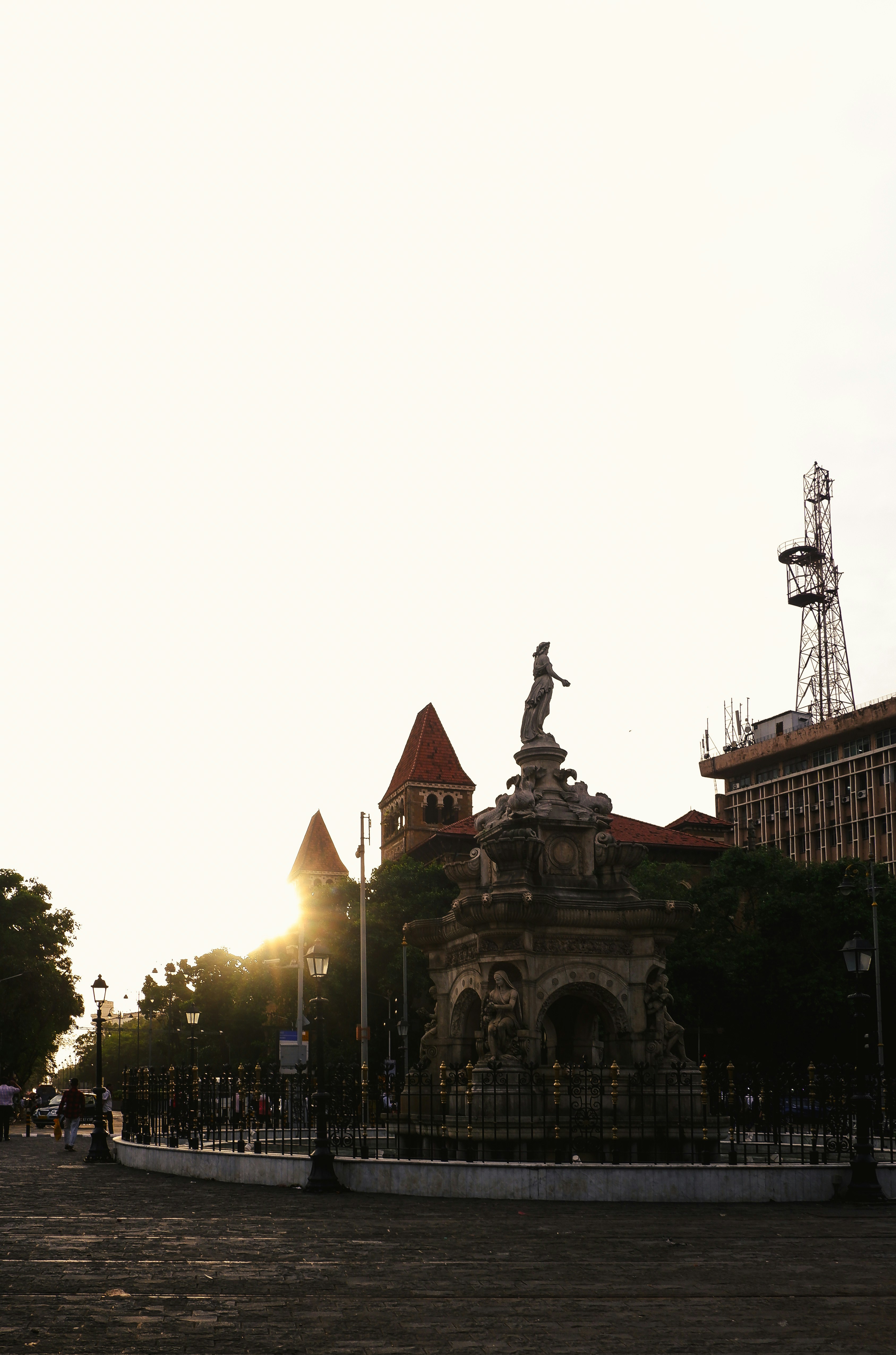 The Flora Fountain in Mumbai at low sun with a tall communications tower.