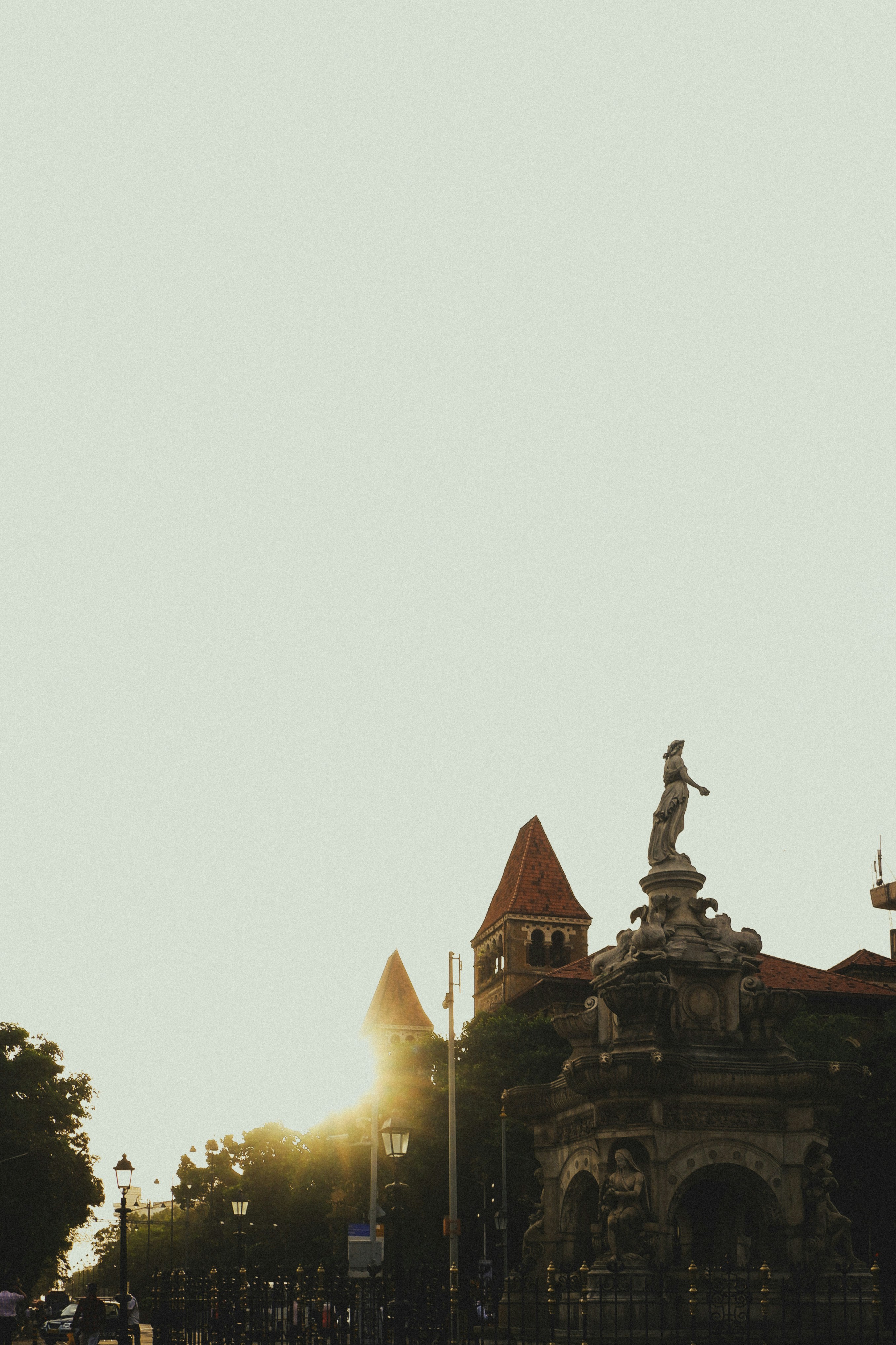 A stone fountain with a statue against a warm sunlit sky in Mumbai.