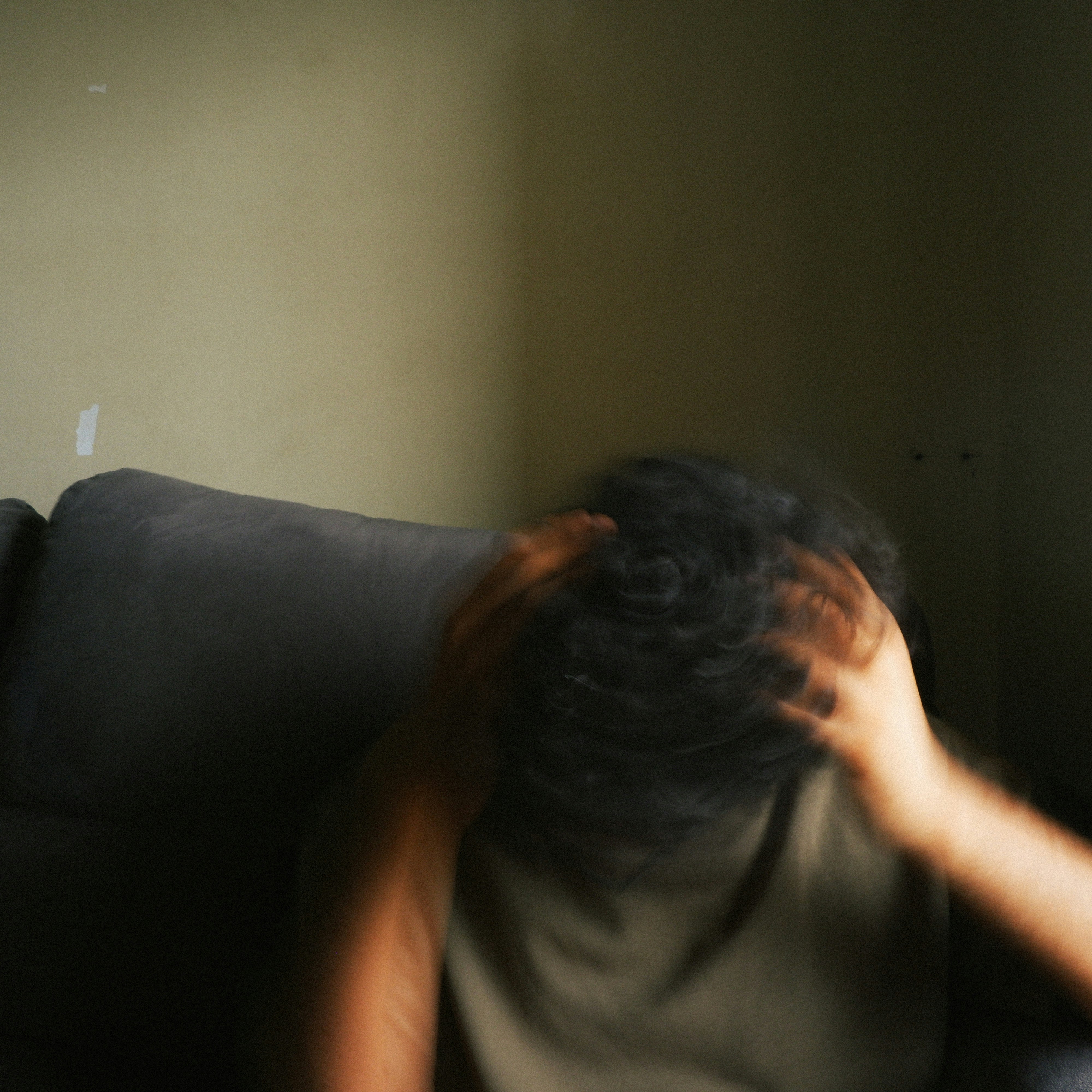 A person with blurred hands touching their head in a dimly lit room.