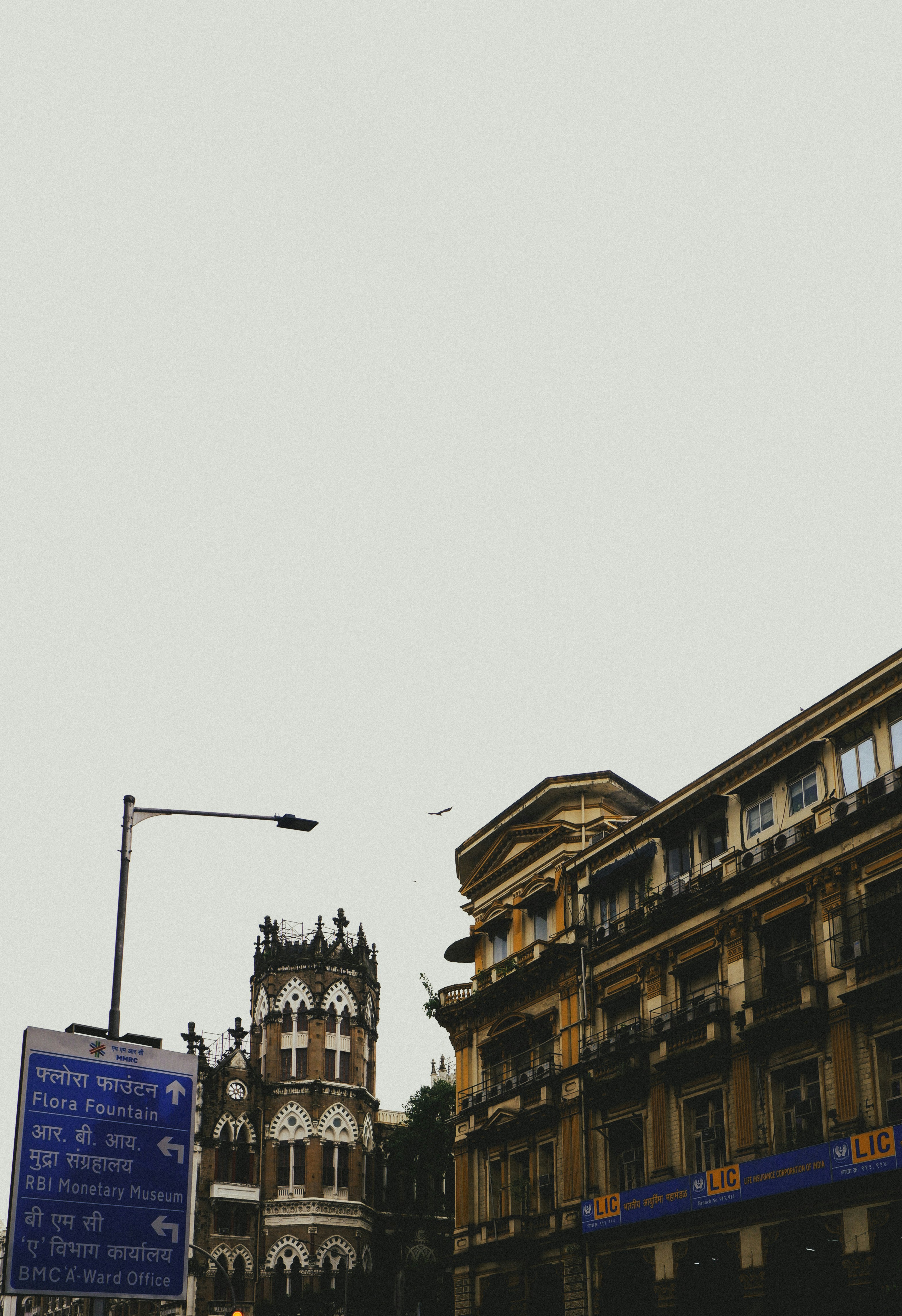 A street sign pointing to Flora Fountain near historic architecture in Mumbai, India.
