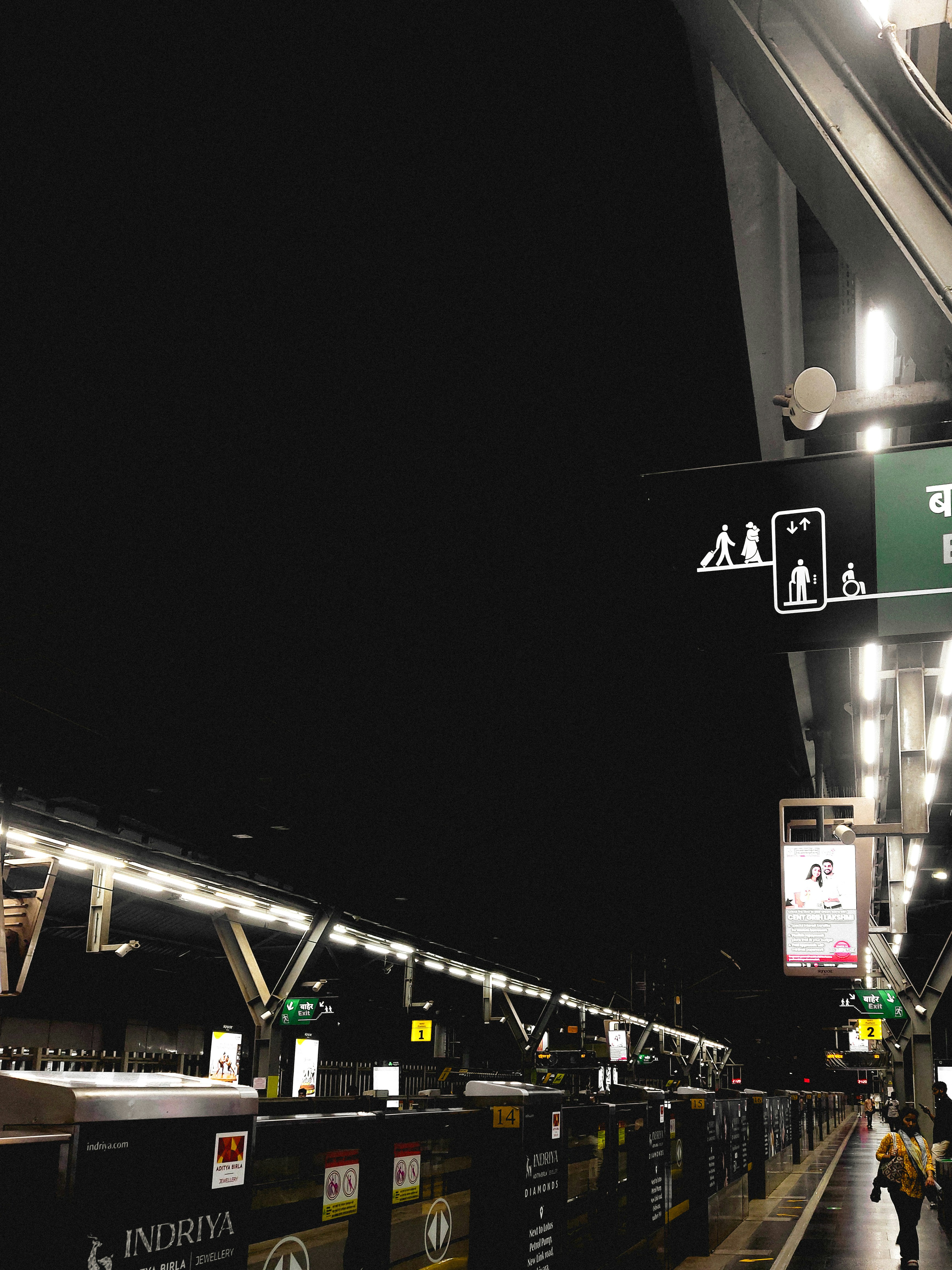 An illuminated metro station platform at night with signage and a person walking.