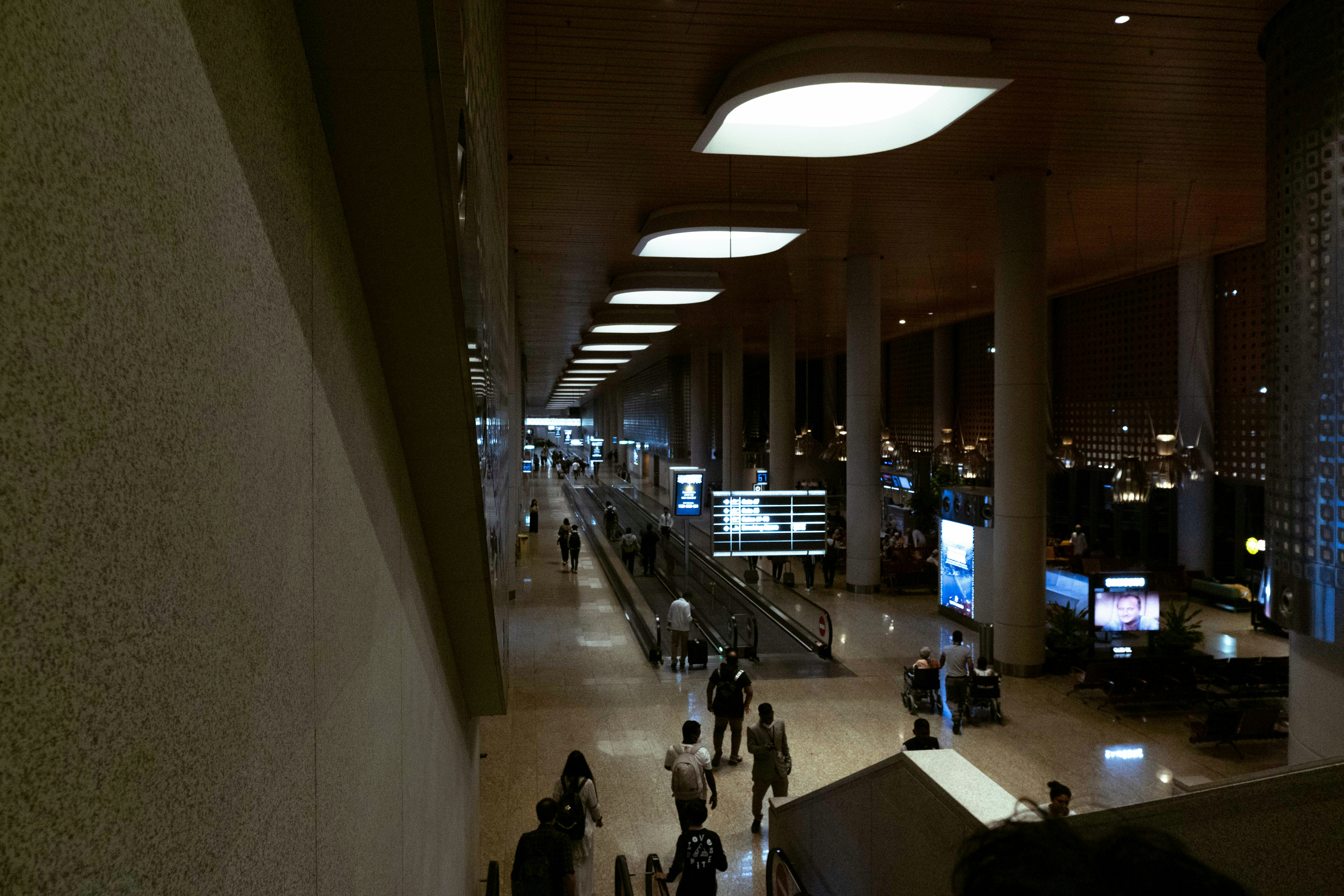 People walking through a modern airport terminal with leaf-shaped ceiling lights.