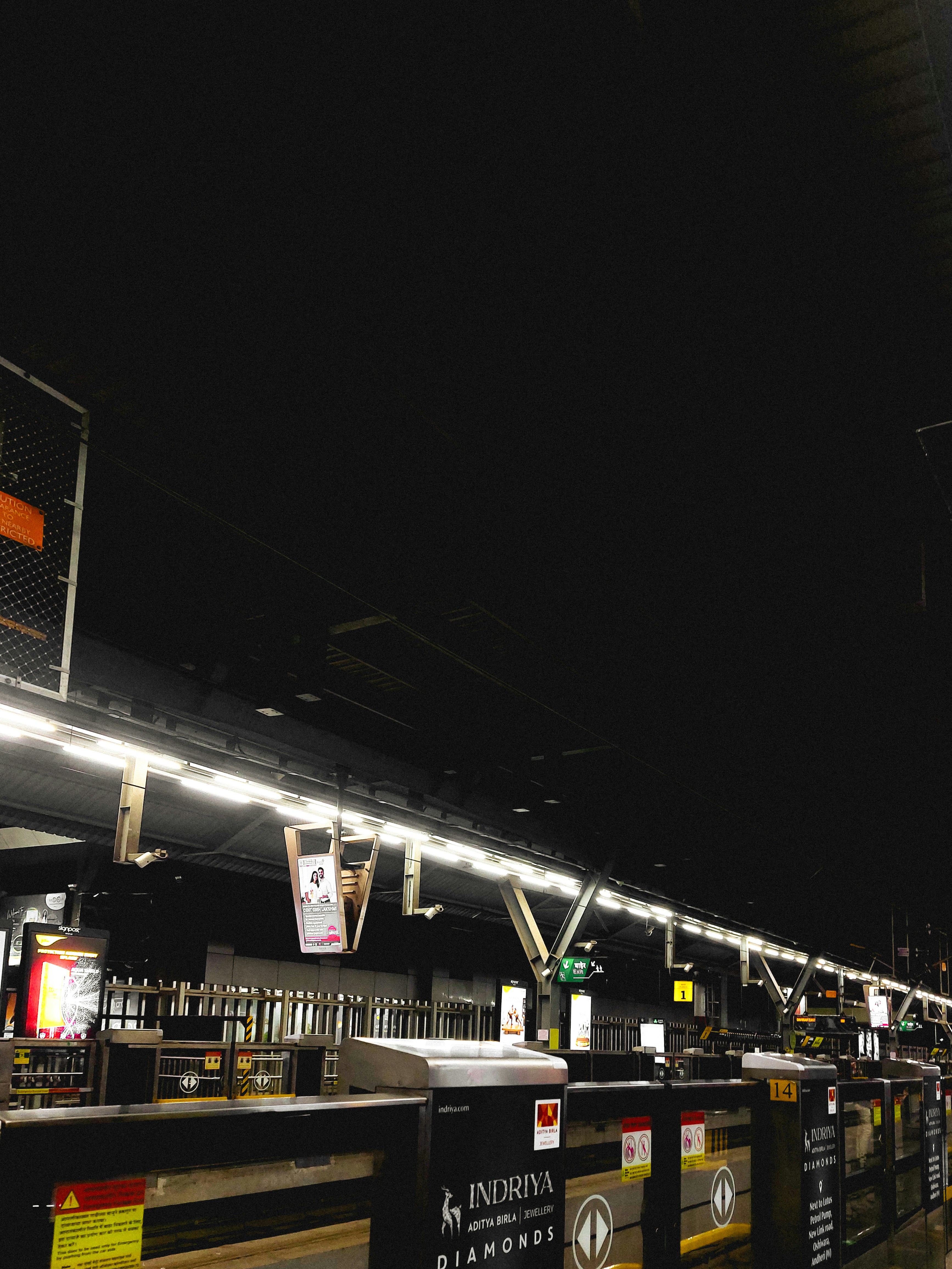 A brightly lit train station platform at night with metal barriers and signage.