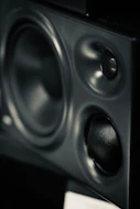 A black studio monitor speaker with a large woofer and two smaller tweeters