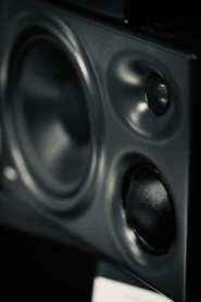 A black studio monitor speaker with a large woofer and two smaller tweeters