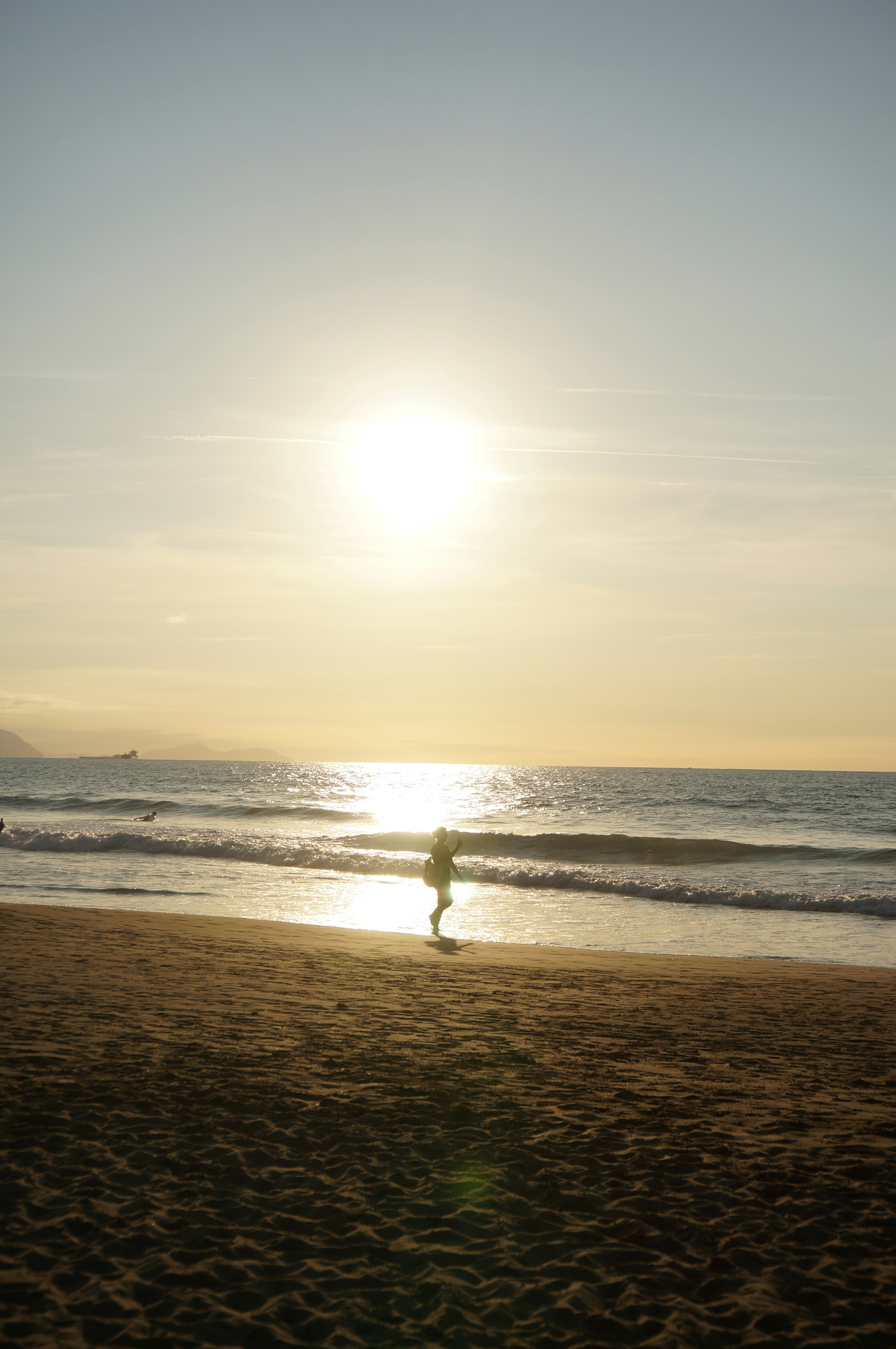 A person in silhouette walking along a sandy beach under a low sun